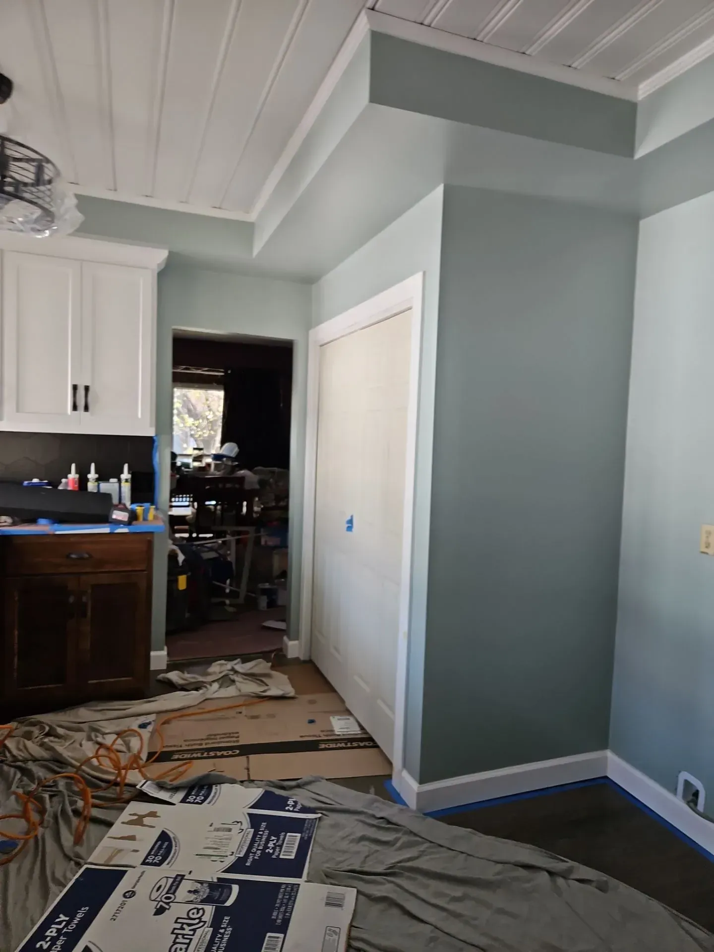 Room with white ceiling, teal walls, and a white closet door, looking into a cluttered room.