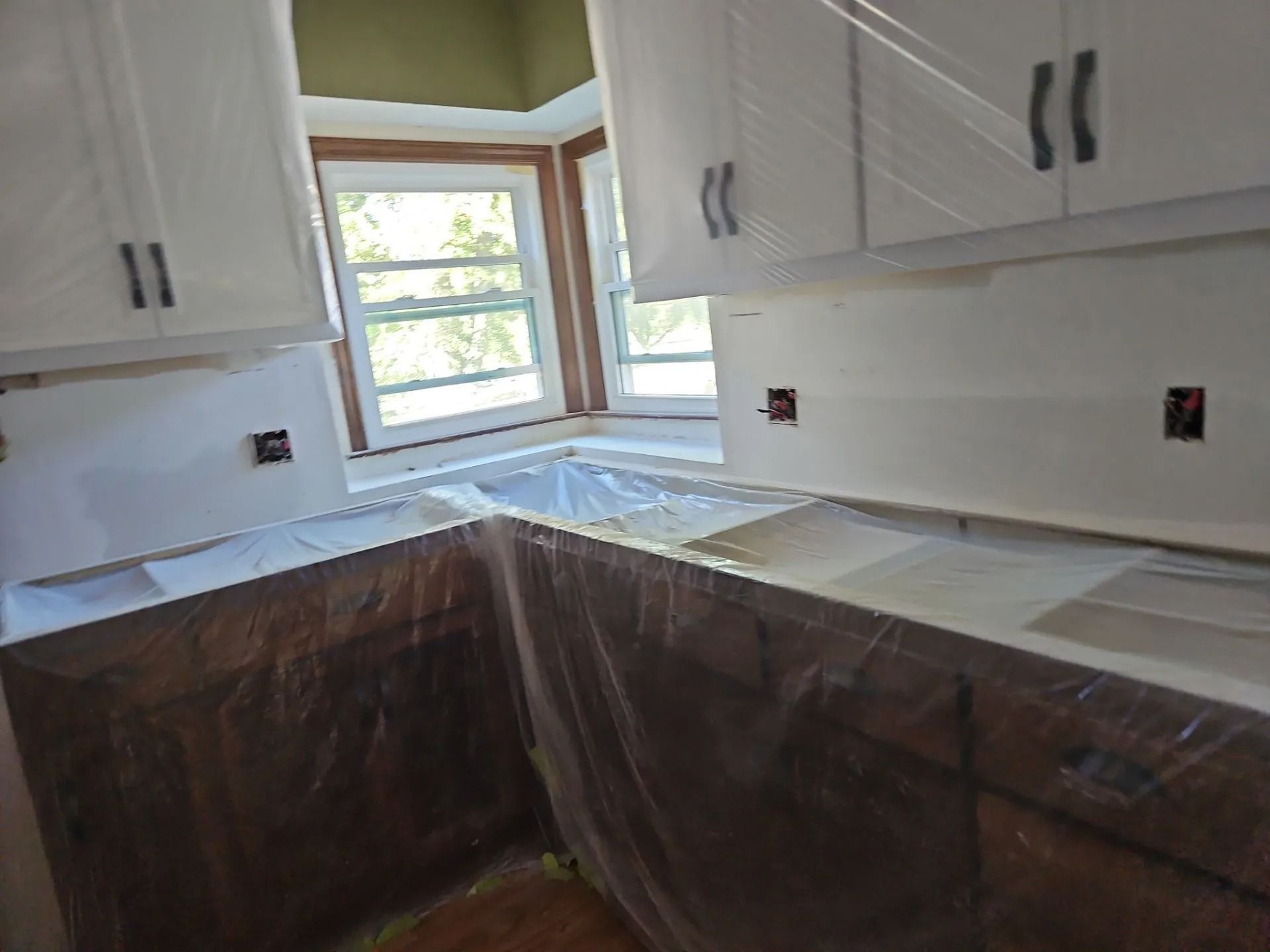 Kitchen under renovation with plastic-covered cabinets and countertops near a window.