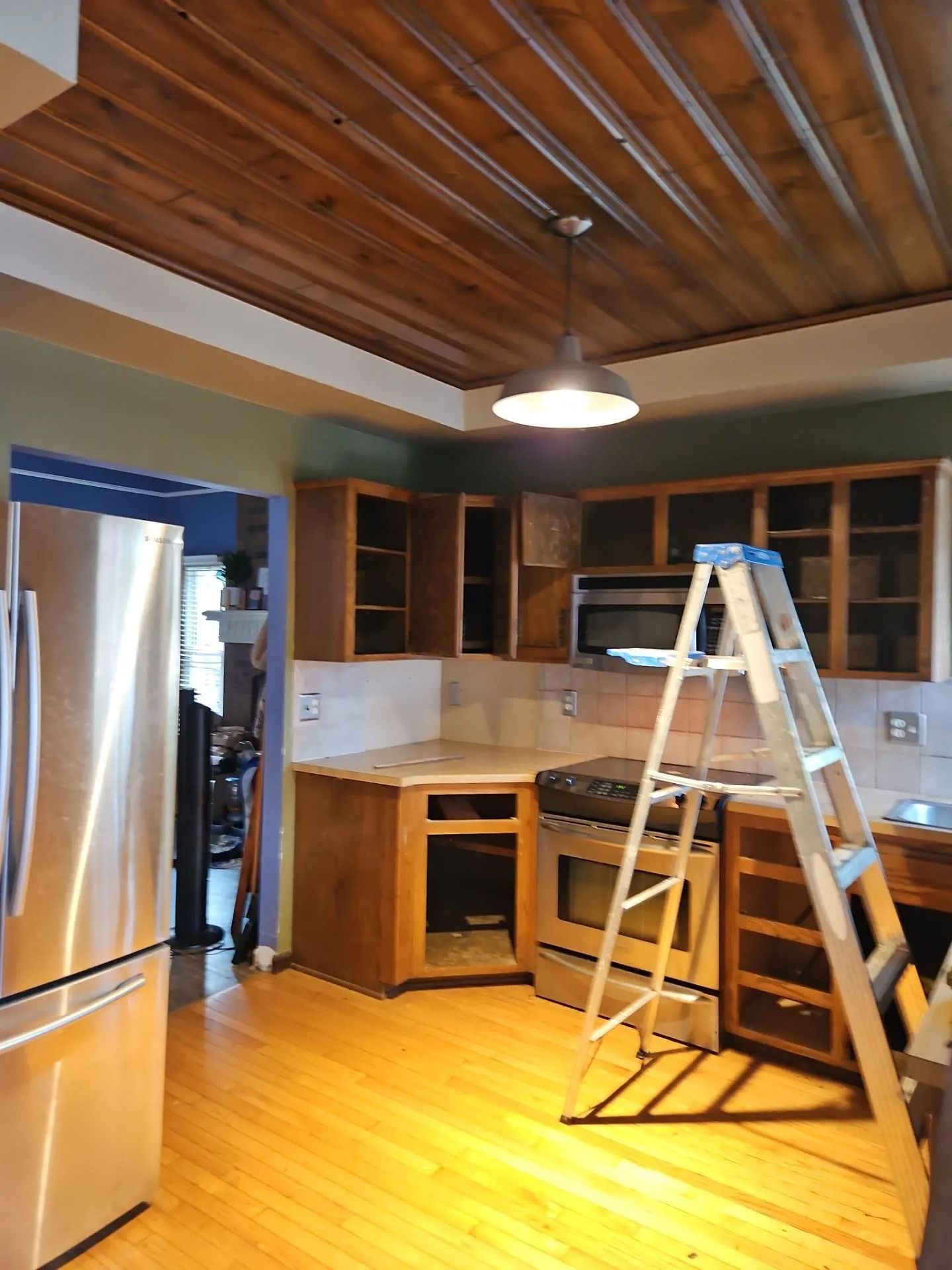 Kitchen undergoing renovation: wood cabinets, stainless steel appliances, ladder, and wooden ceiling.