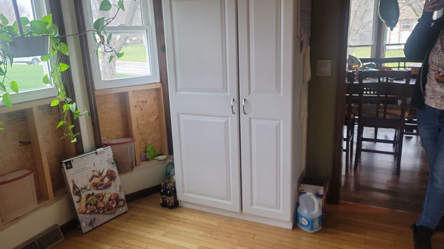 White pantry cabinet in a kitchen with a partially unfinished wall; a person stands nearby.