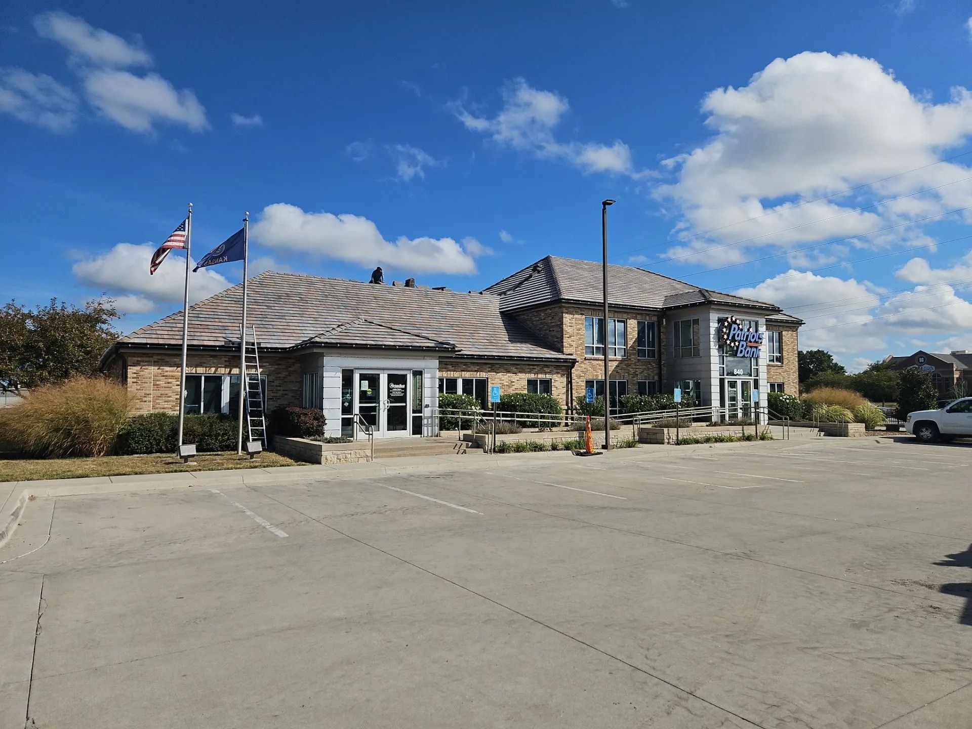 Two-story brick building with flags and a parking lot under a blue sky with clouds.