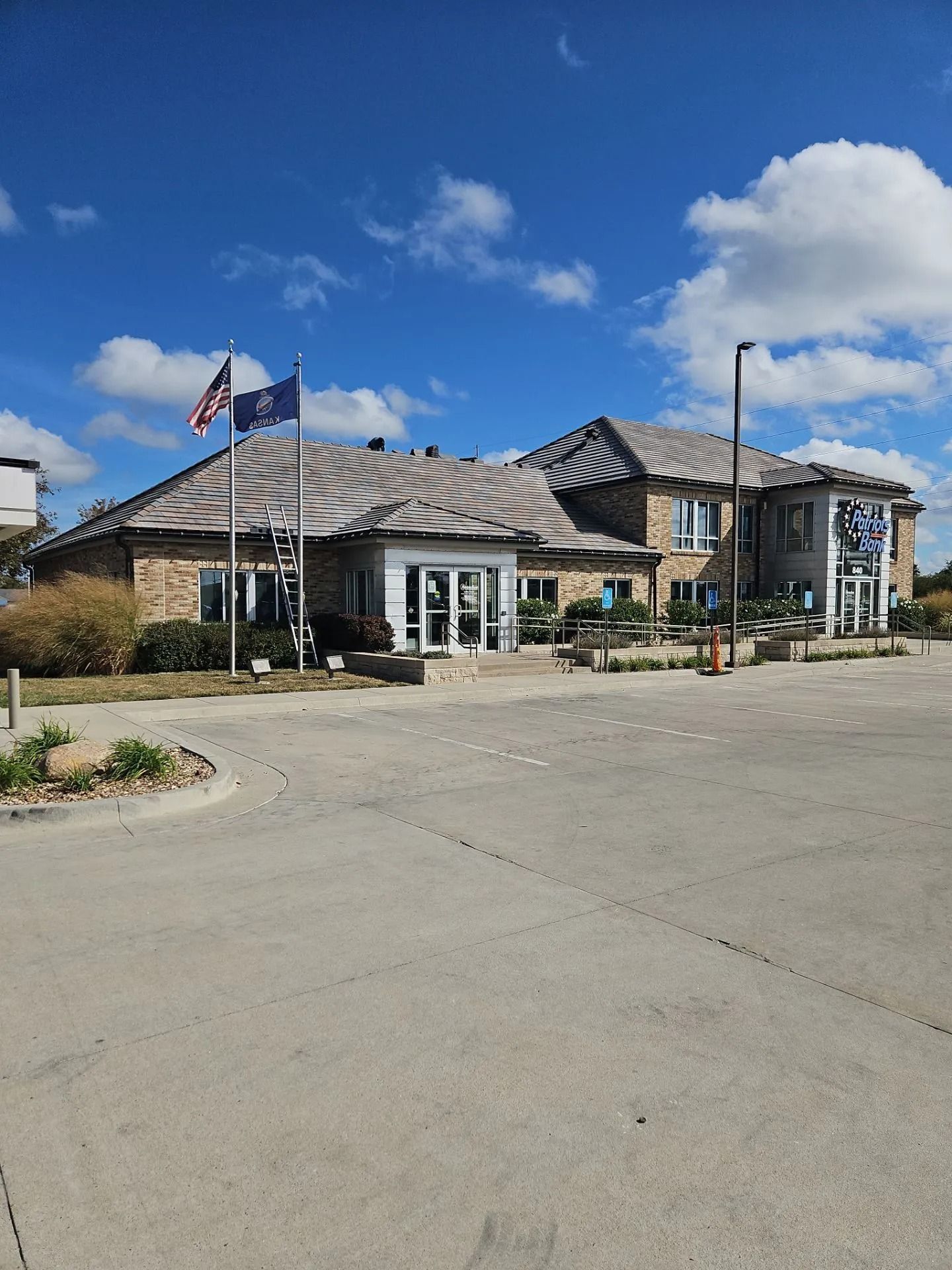 Building with brick exterior, flags flying, clear sky, and a paved parking area.