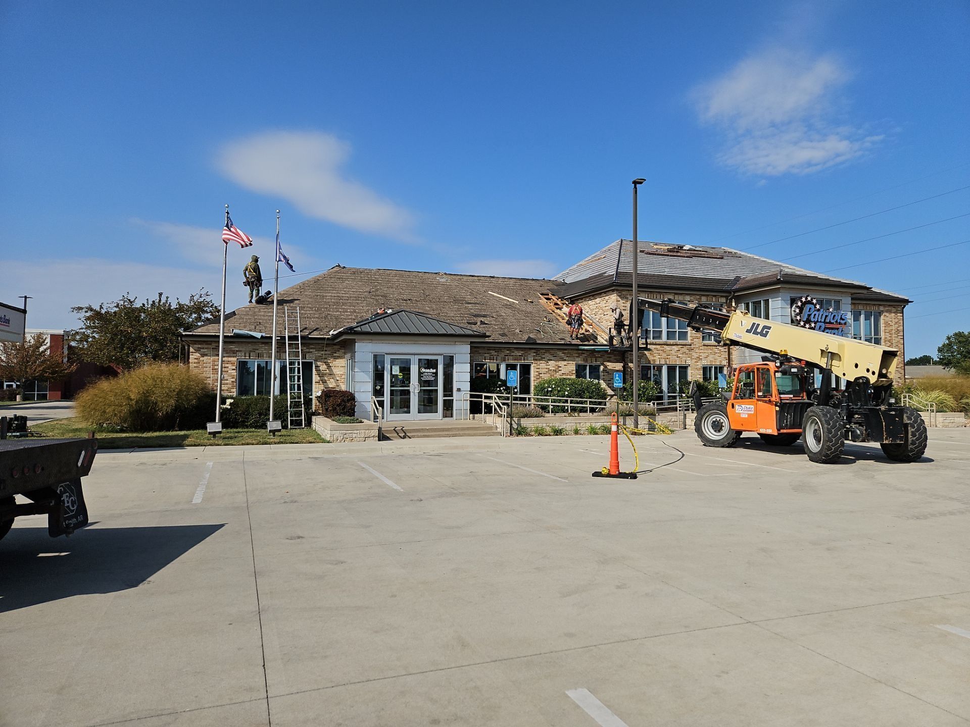 Building with flags, construction lift, and parked vehicles under a blue sky.