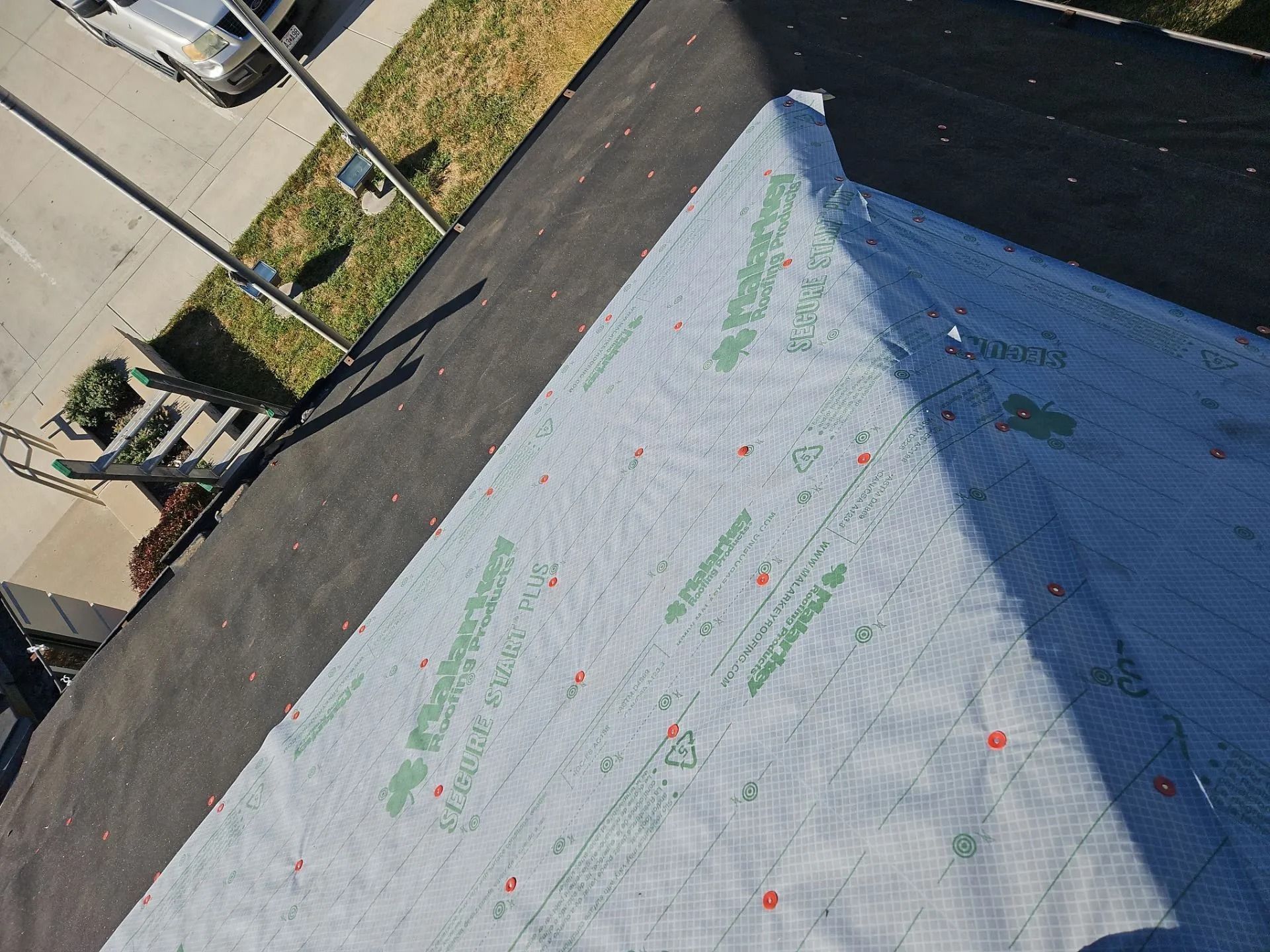 Roofing underlayment installed on a building, with a street and parked car visible.