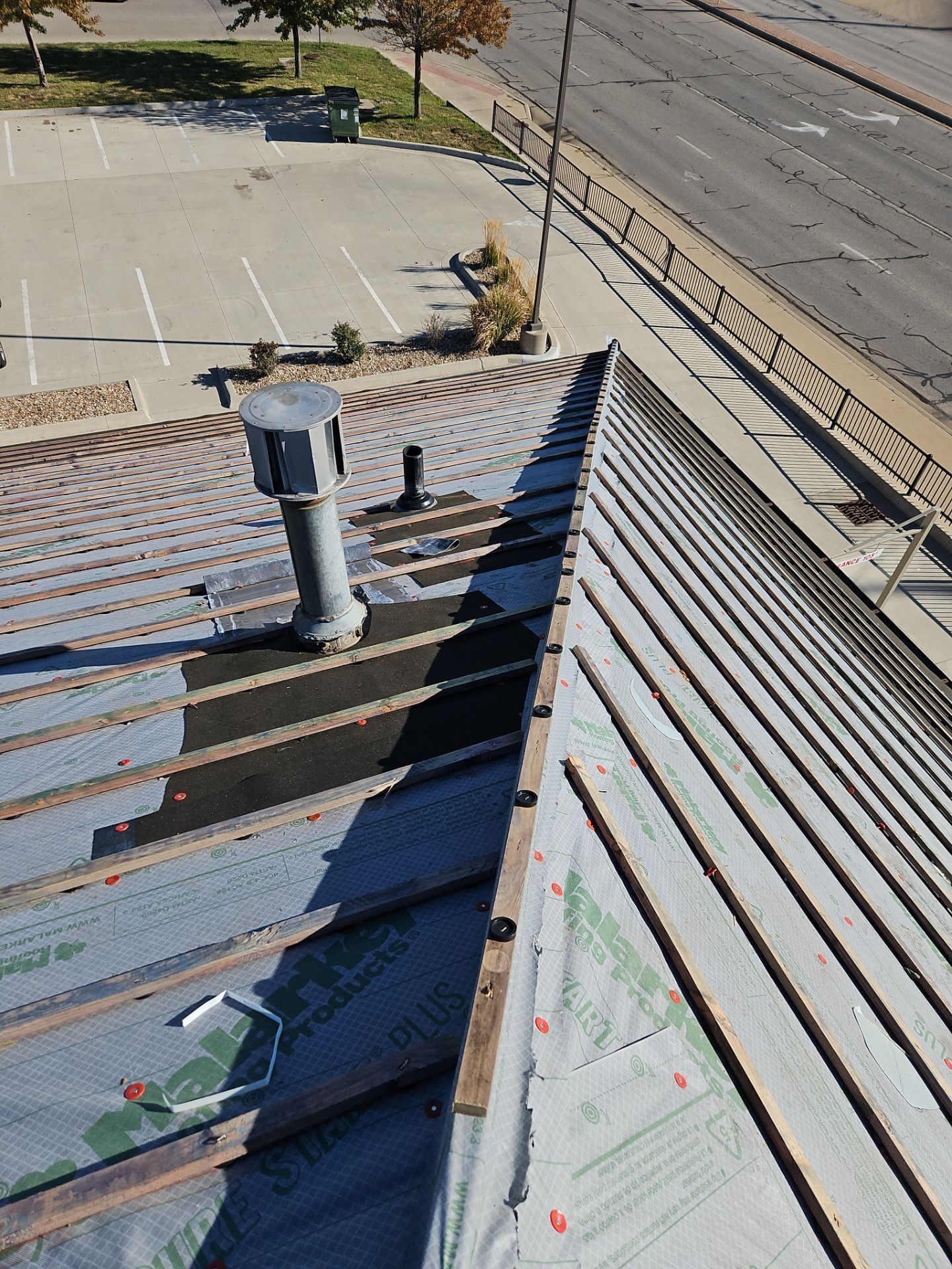 View of a rooftop with ventilation and metal strips, asphalt surface, and street in background.