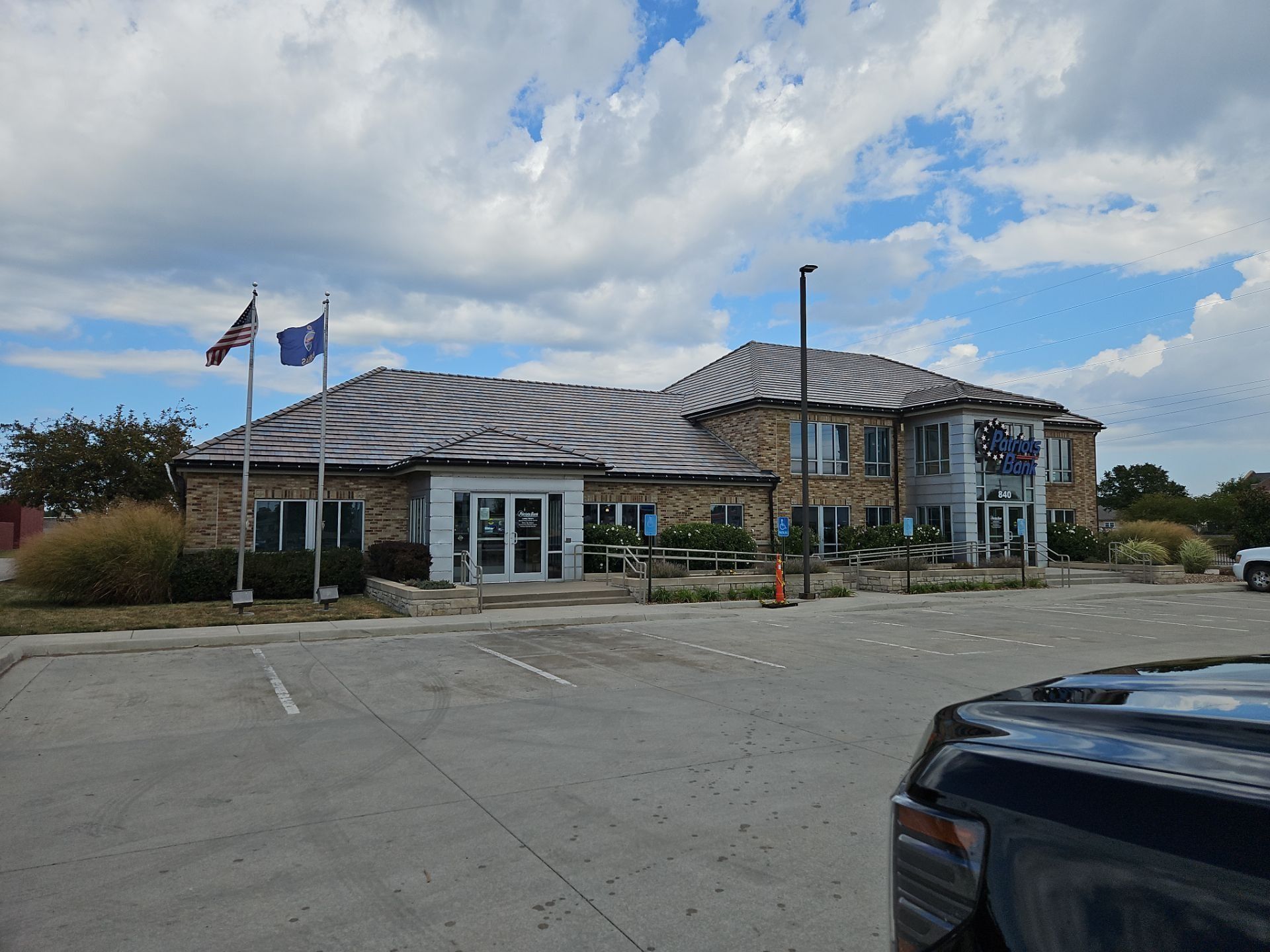 Bank building with brick facade, flags, and parking lot under a cloudy sky.