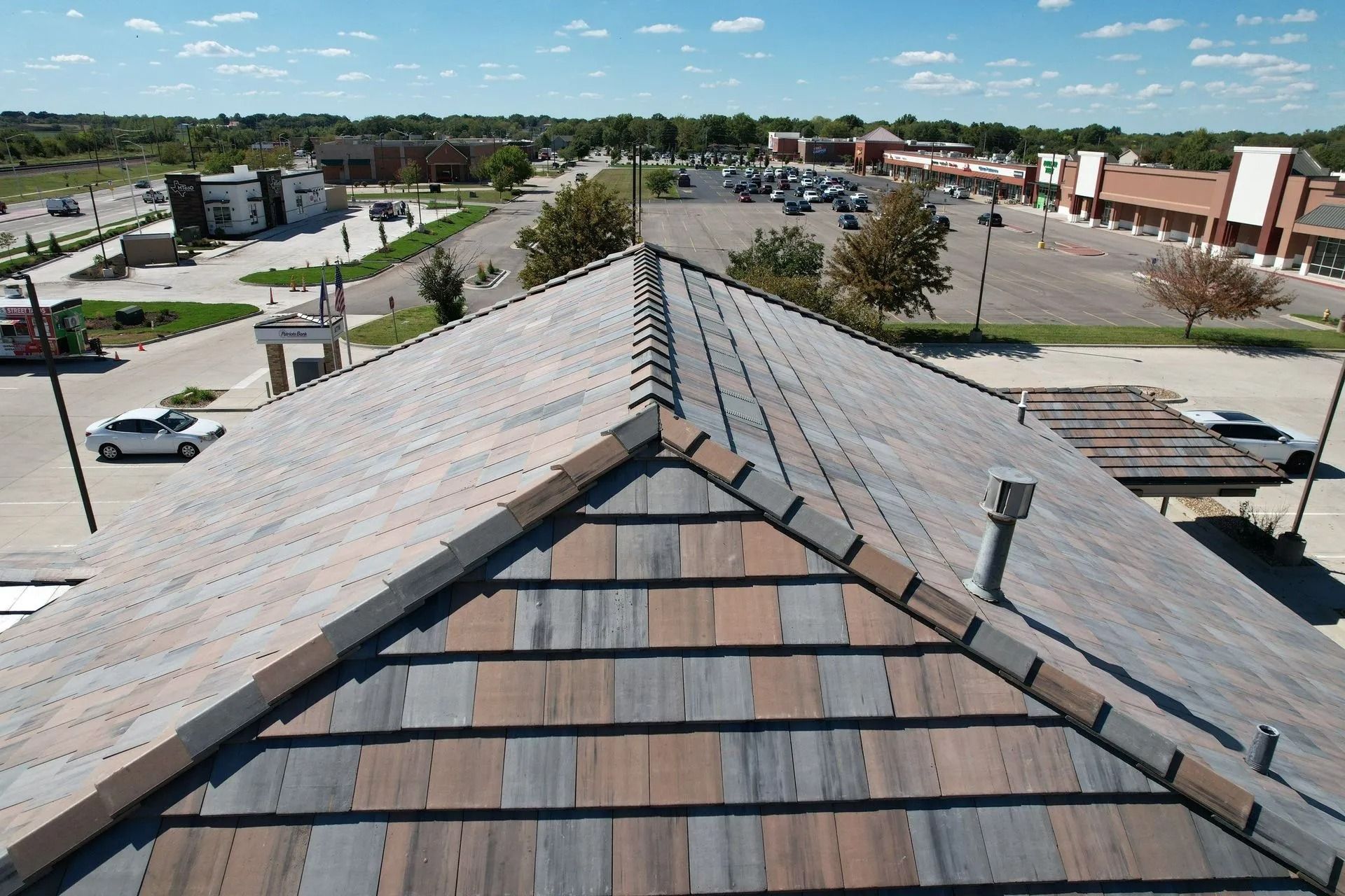 View from a building roof with multi-colored tile roofing, looking out onto a parking lot and other buildings under a blue sky.