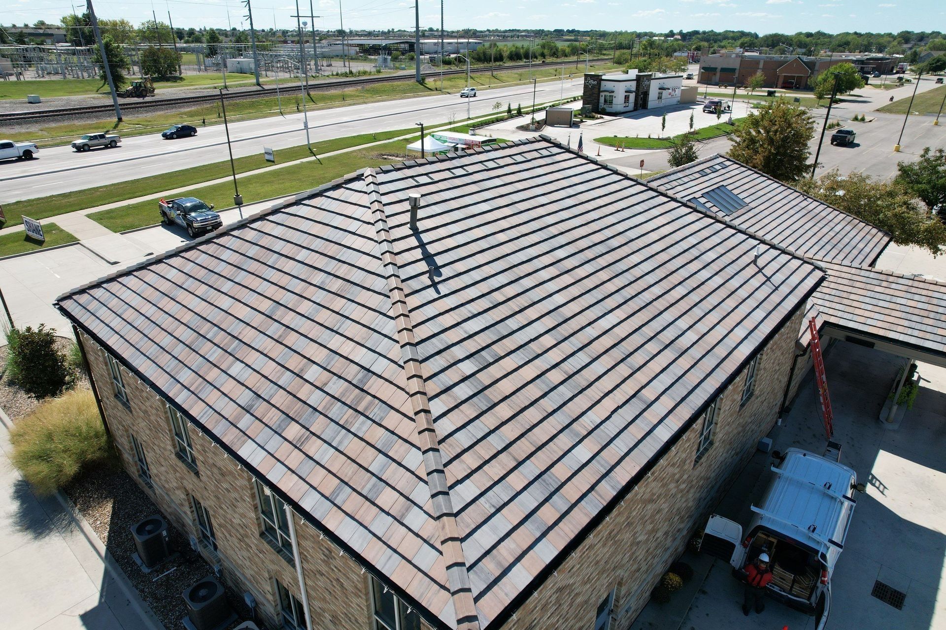 Overhead view of a building with a multi-tone tile roof, next to a road, and utility area.