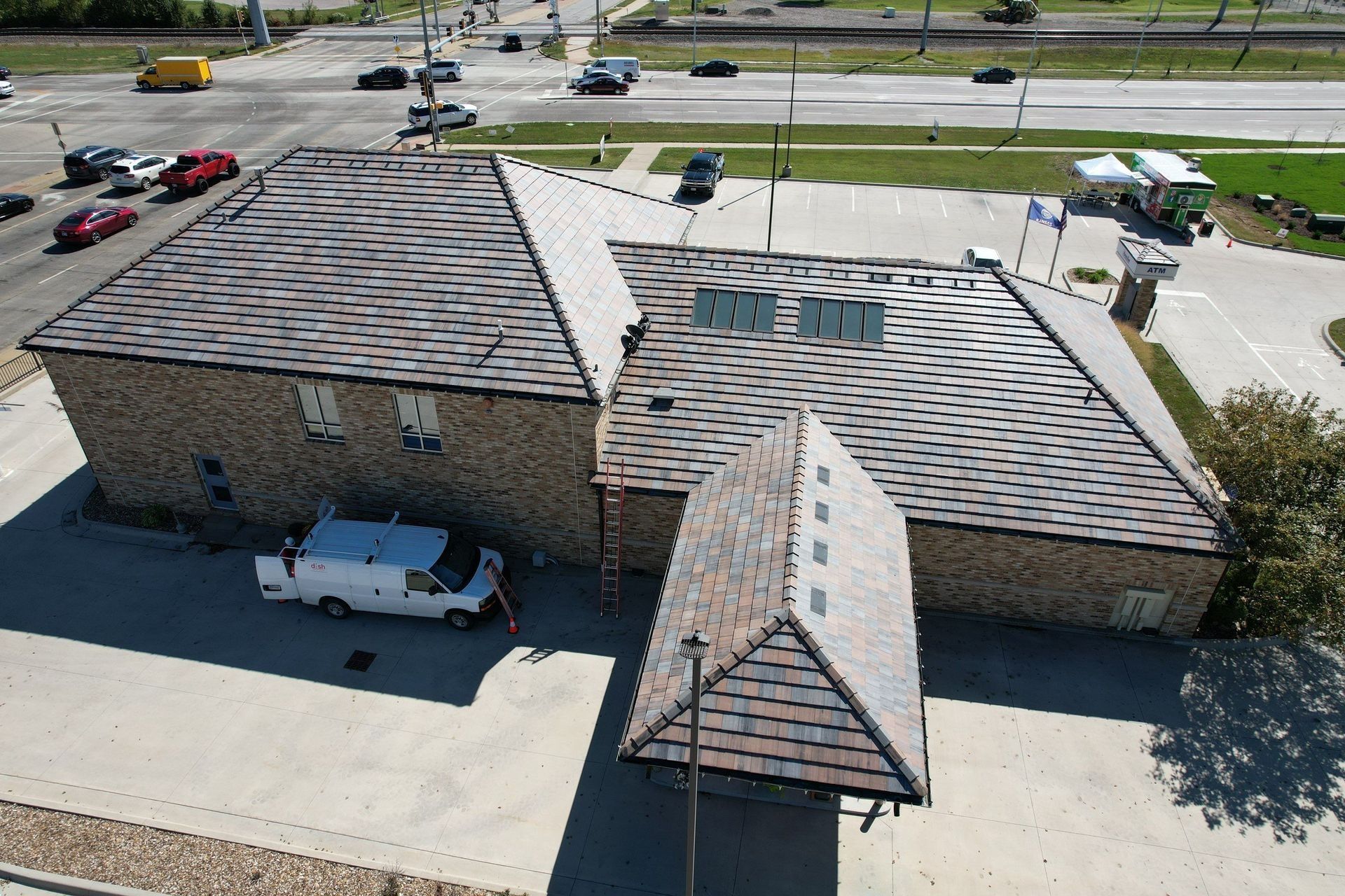 Aerial view of a building with a newly shingled roof, brick walls, and a parking lot. A white van is parked near the building.