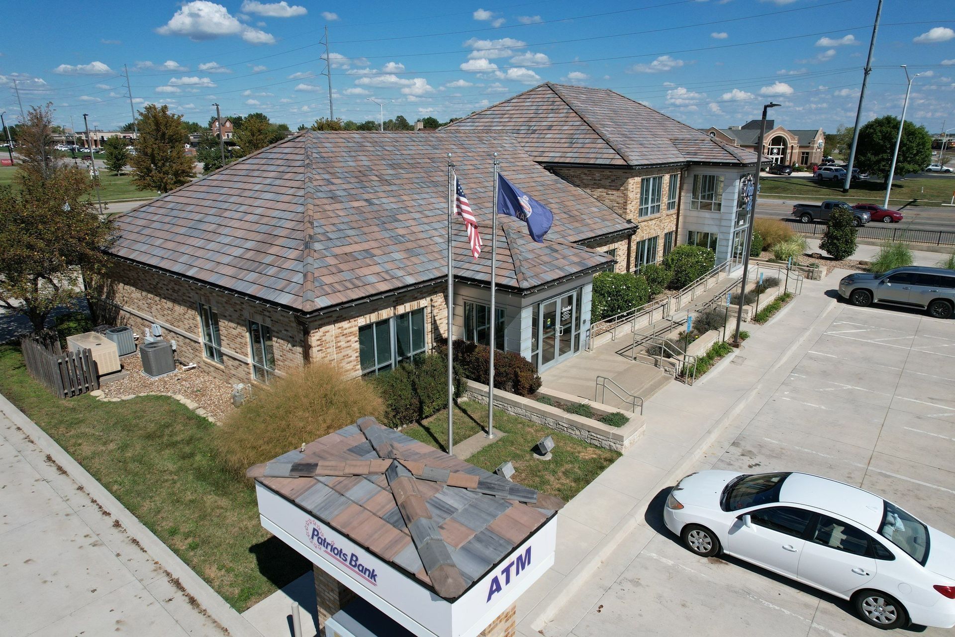 Building with flagpoles and an ATM in front; car parked nearby.