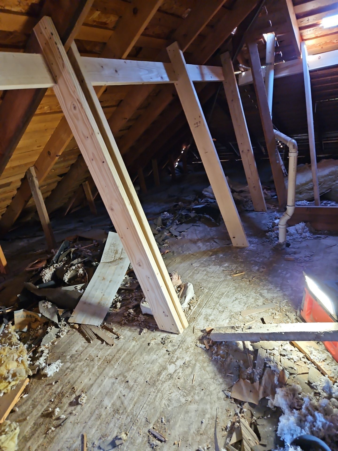 Attic interior showing wooden support beams angled against the rafters. Insulation and debris cover the floor.