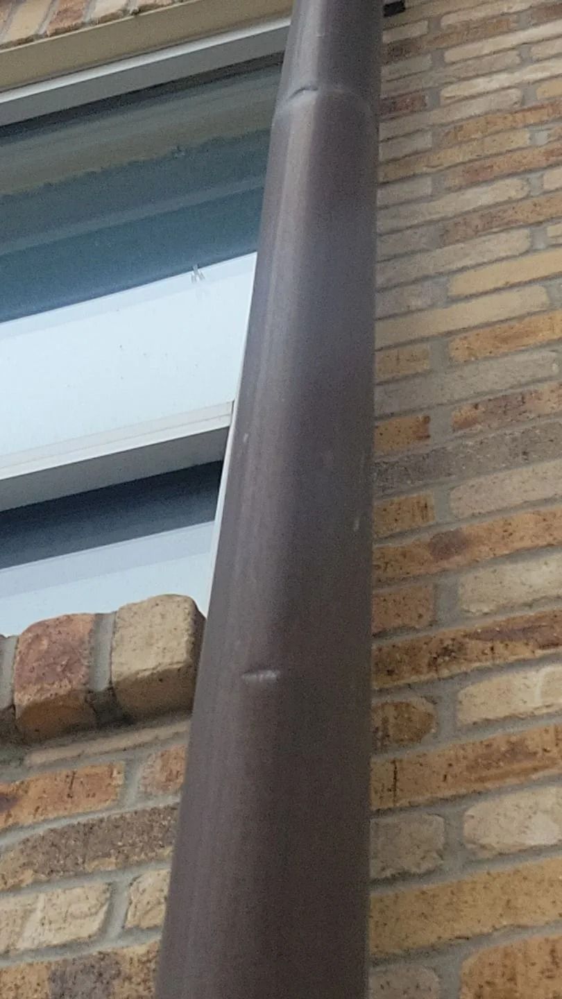 Brown downspout on a brick building beside a window.