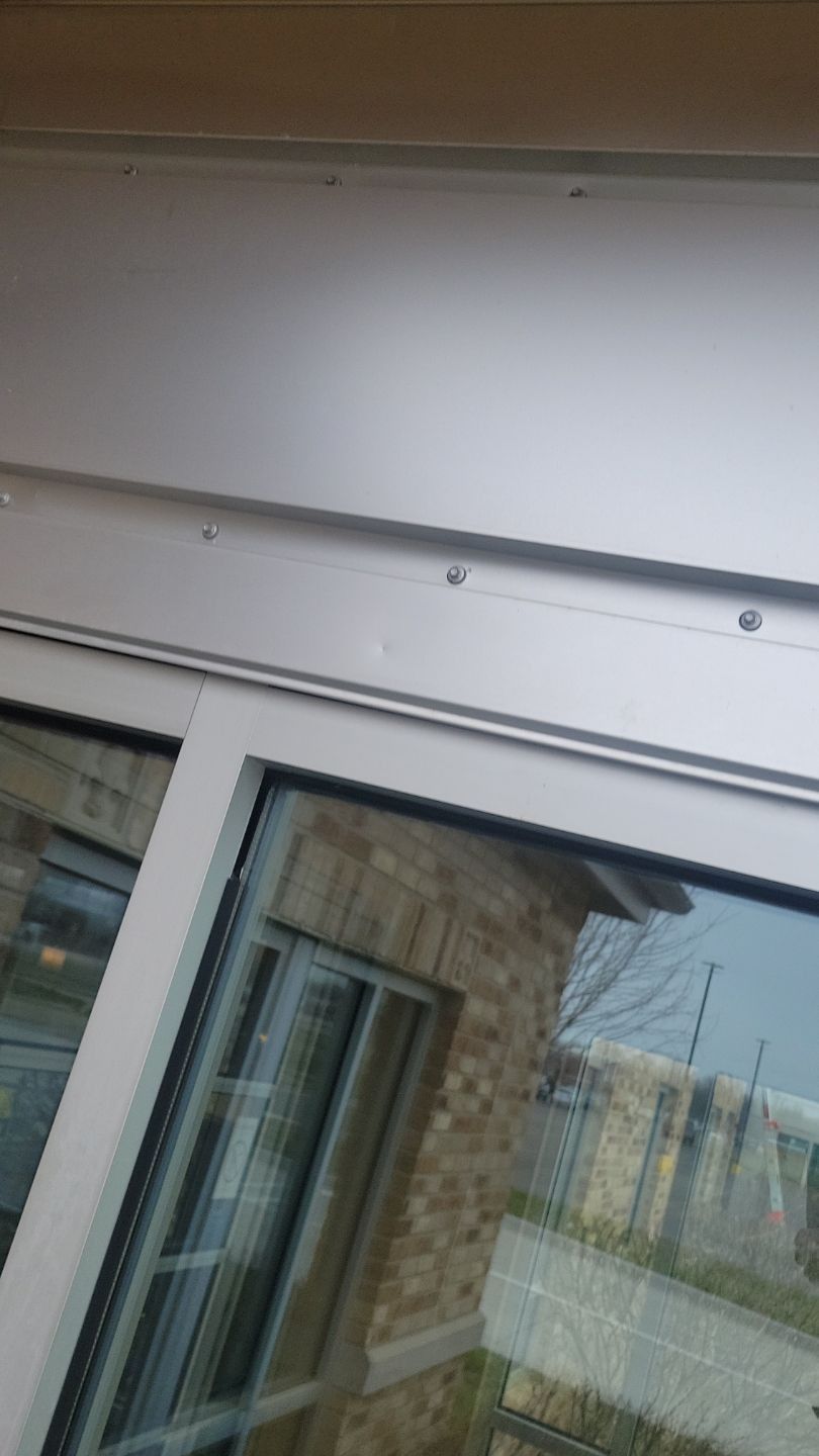 Sliding glass door frame. Silver frame, clear glass reflecting a brick building and greenery.