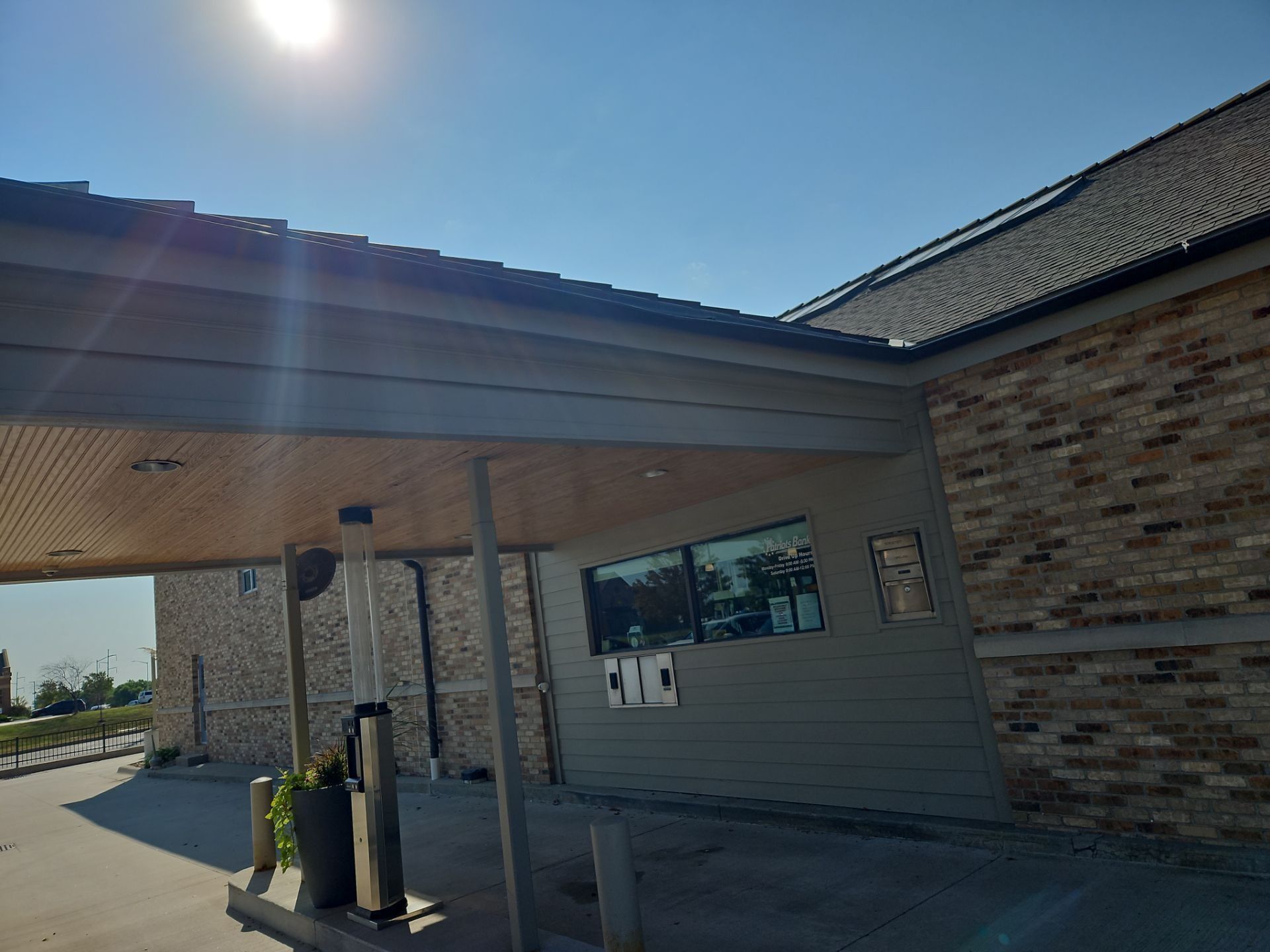 Bank building with drive-through canopy. Sun is shining. Brick exterior, gray roof.