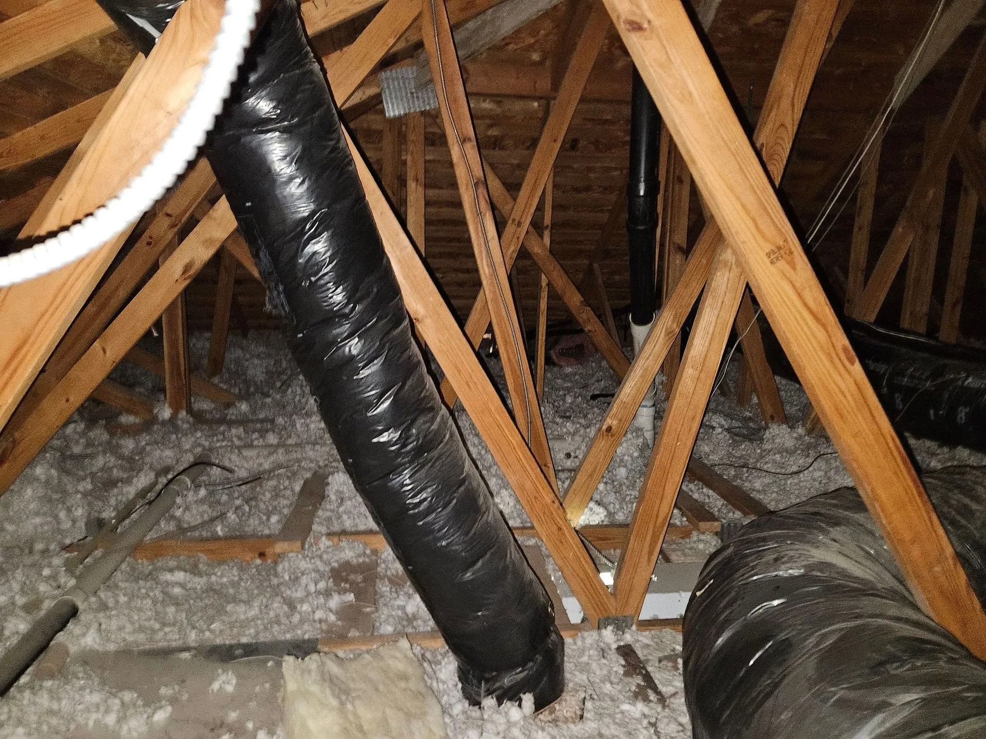 Attic with wooden rafters, black insulated ductwork, and insulation.