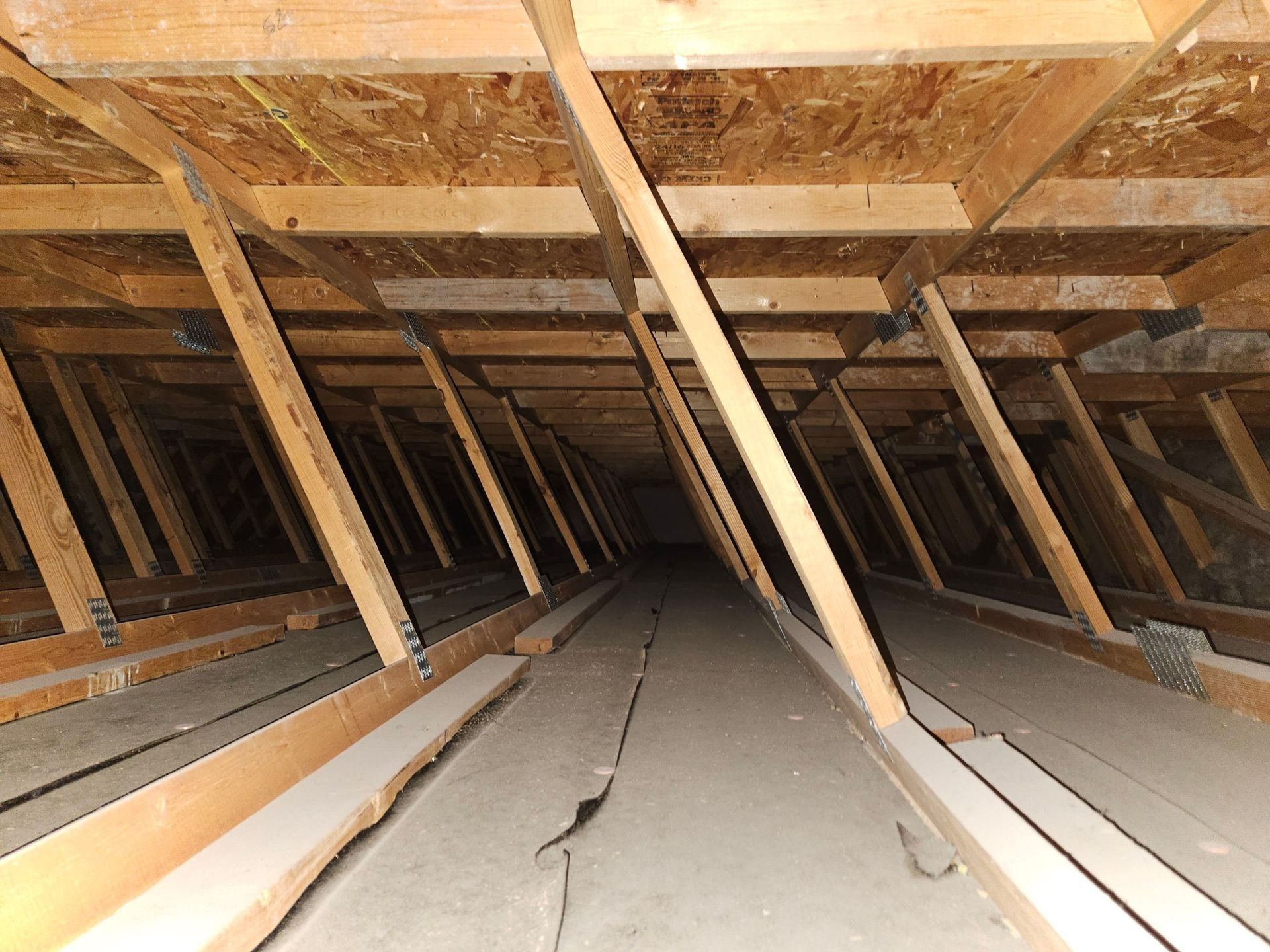 Interior view of an attic with wooden rafters and sheathing, angled supports, and a dark space ahead.