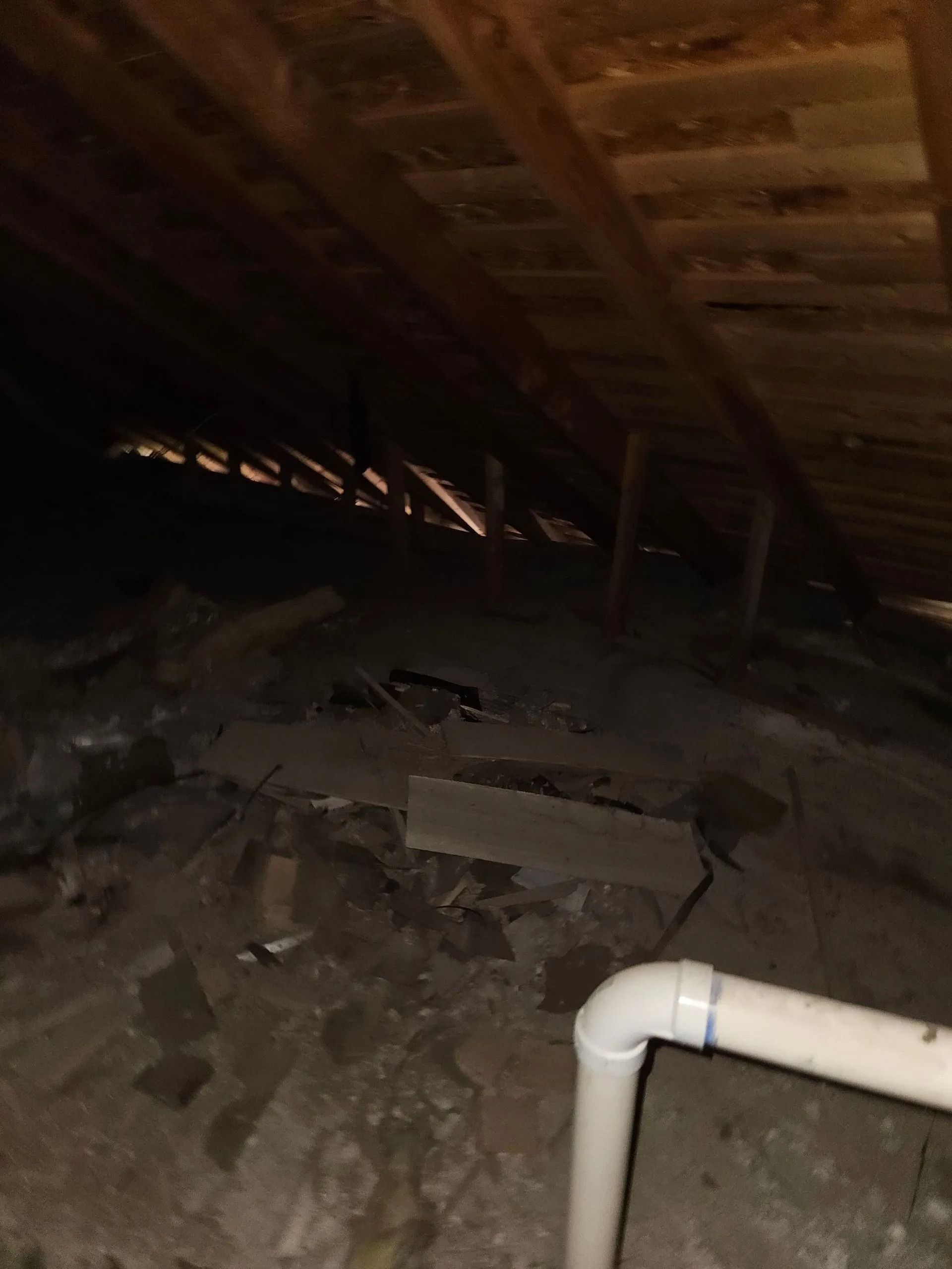 Dark attic interior with visible wooden beams and a white pipe.