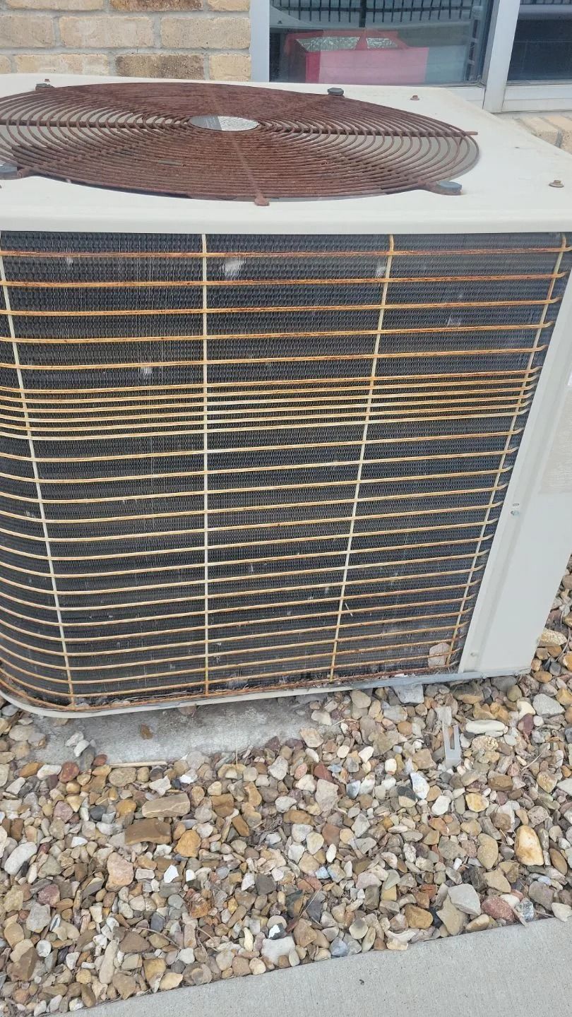 Outdoor air conditioning unit with rusted top and dirty fins, sitting on gravel.