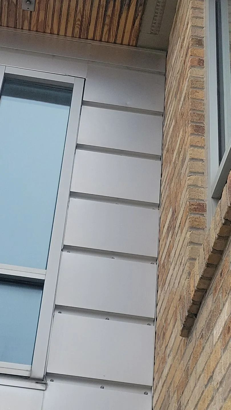 Exterior building corner with gray metal siding and brick wall.
