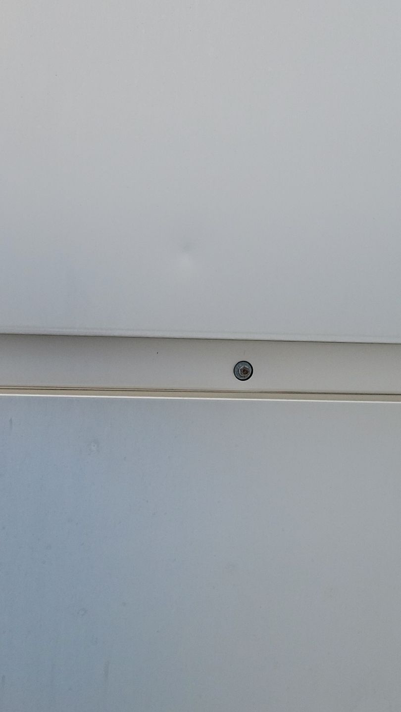 Close-up of a white surface with a visible screw in the middle of a seam.