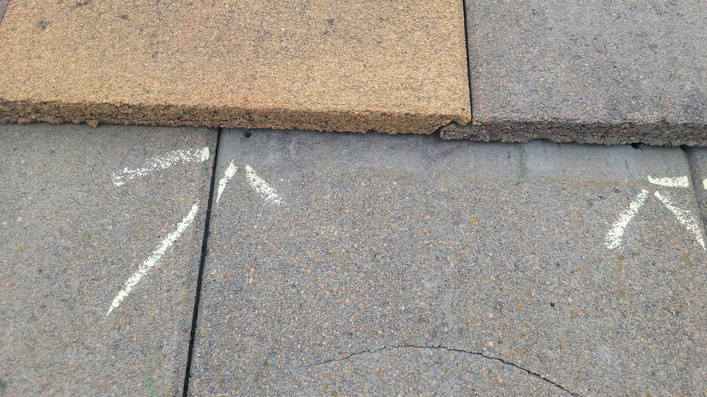 Close-up of weathered gray and tan roof tiles with white chalk arrows indicating direction.
