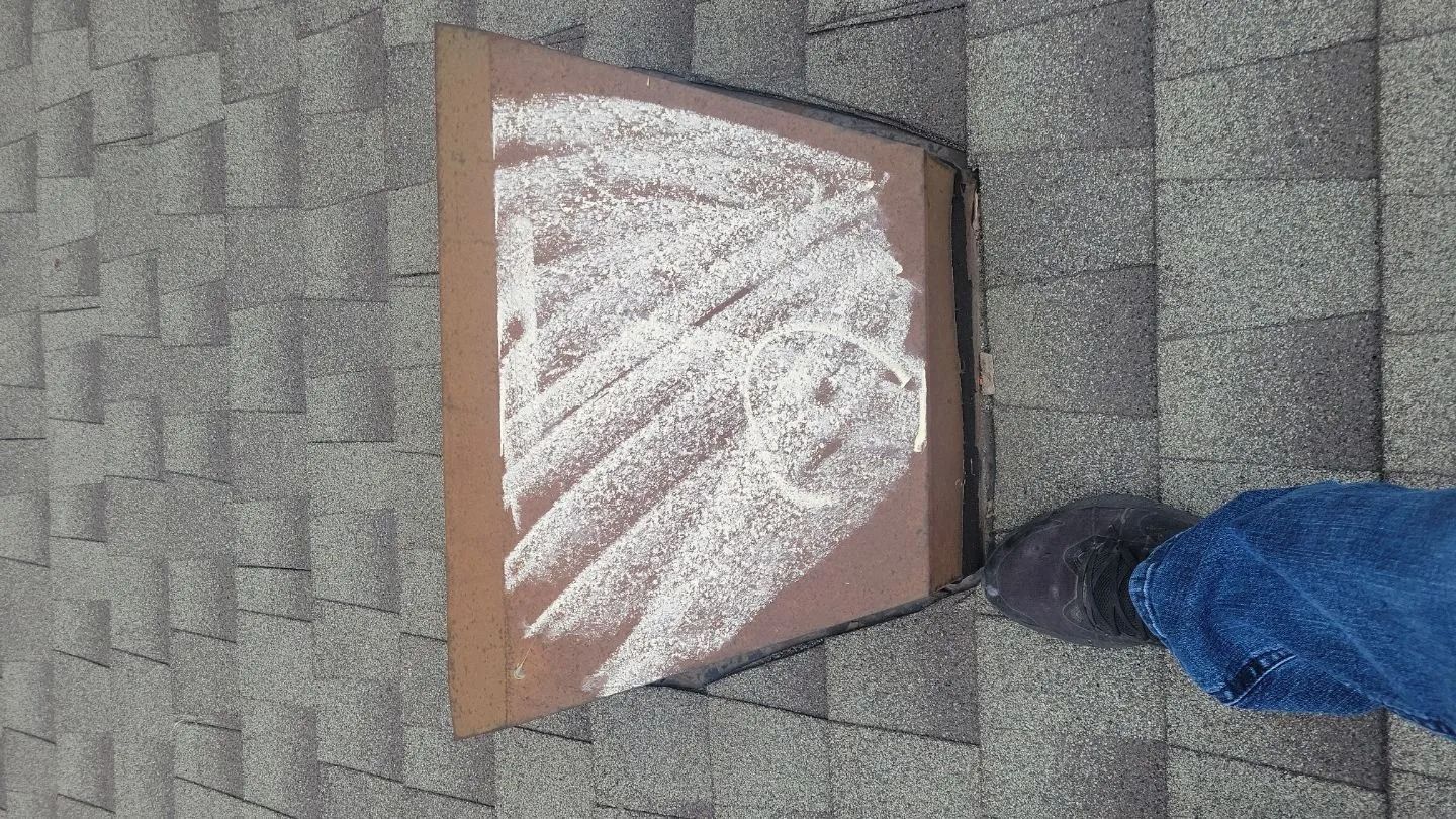 Cardboard template on roof shingles, marked with chalk. A person's leg and foot are partially visible.