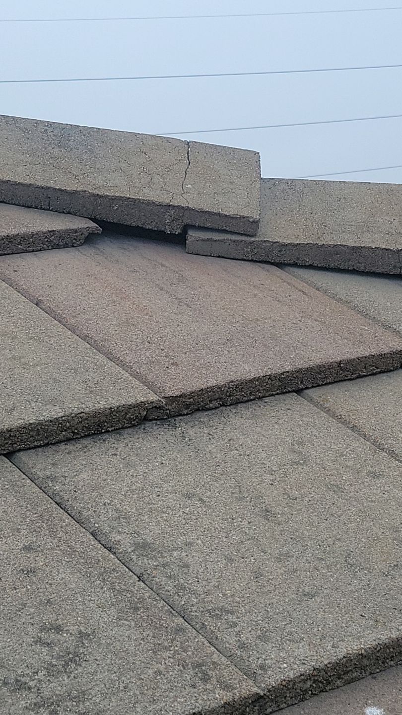 Close-up of gray rectangular roof tiles overlapping on a building, under a white backdrop.