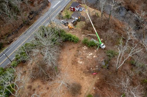 Aerial view of a roadside worksite with a crane, equipment, and cleared ground beside trees.