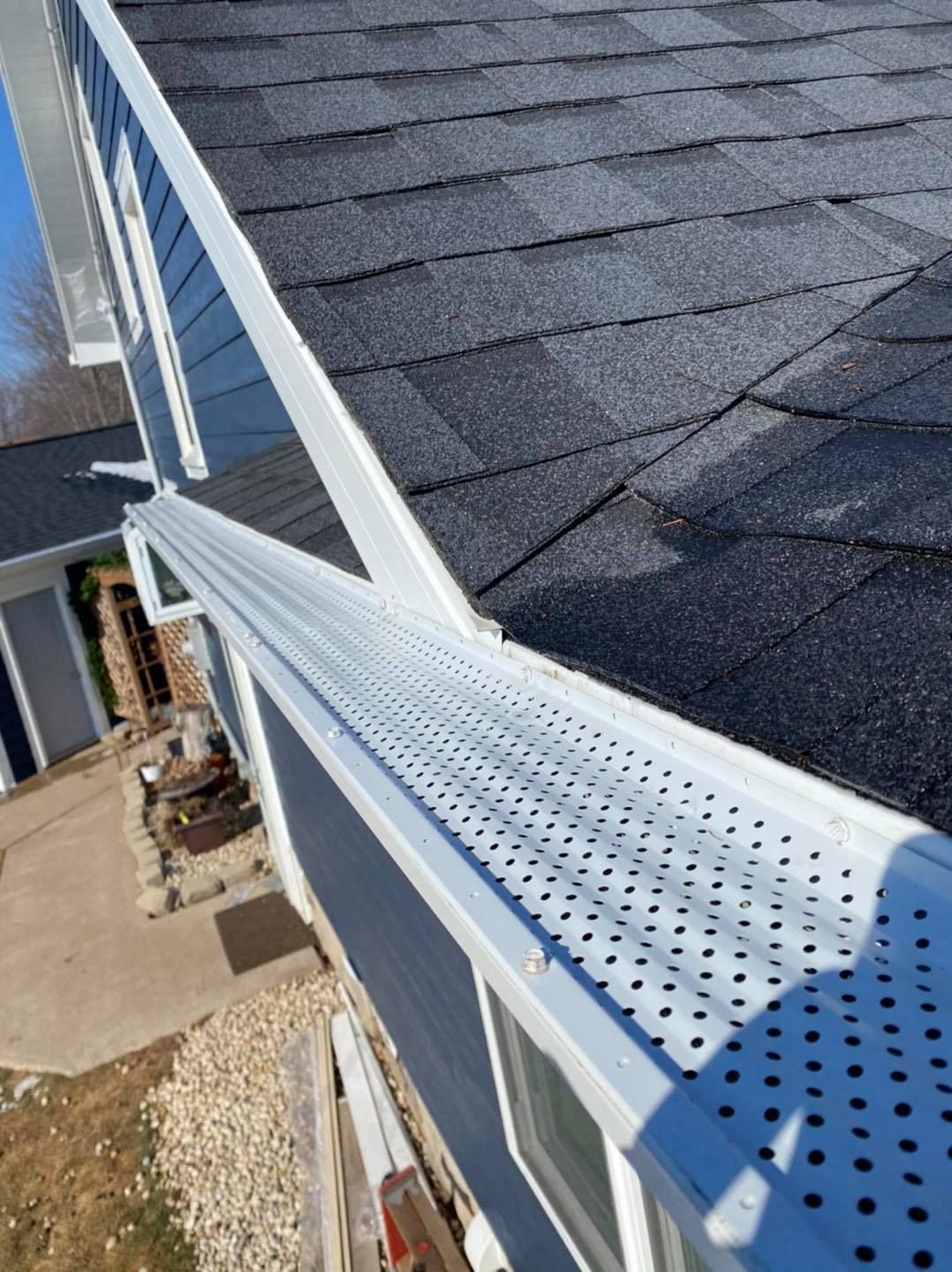 A white gutter on the side of a house with a black roof.