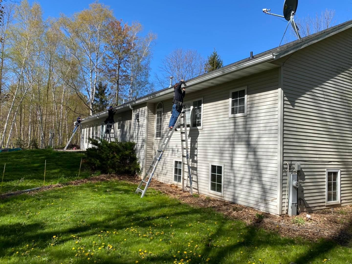 A man is standing on a ladder on the side of a house.