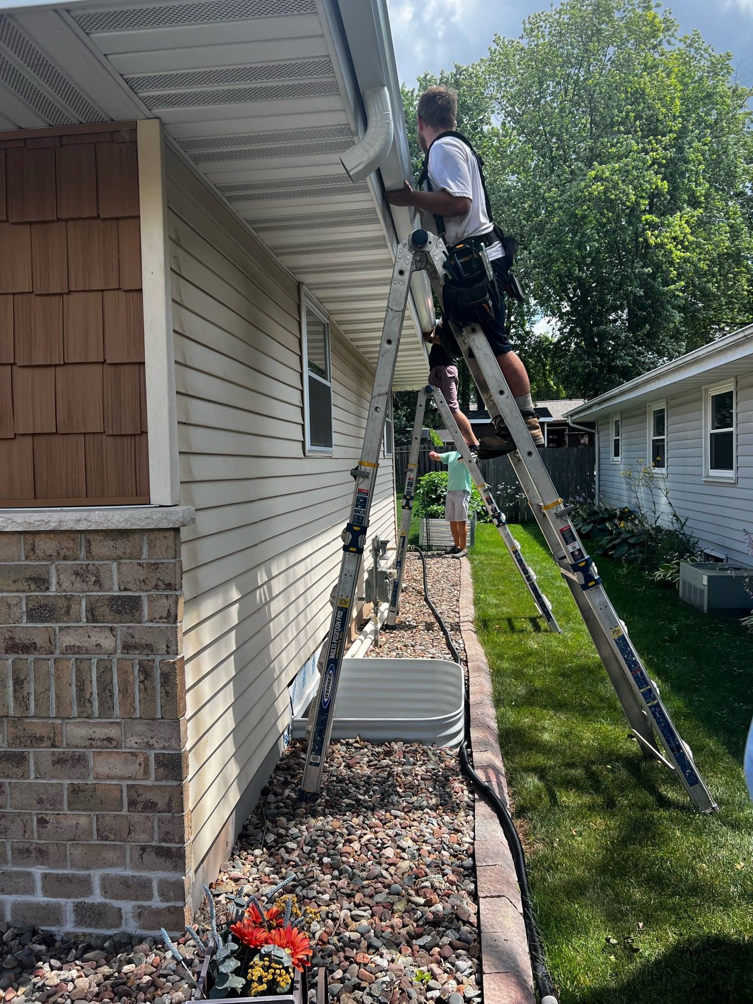 A man is standing on a ladder working on the side of a house.