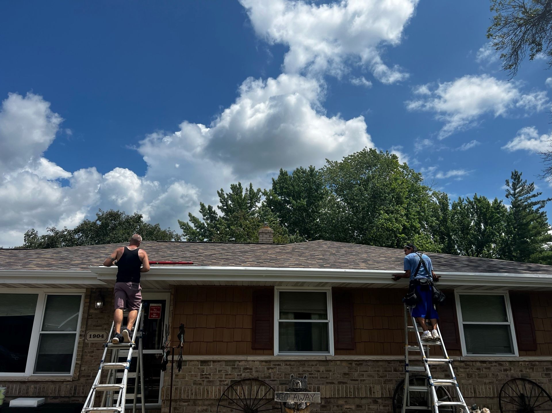 Two people are working on the roof of a brick house.