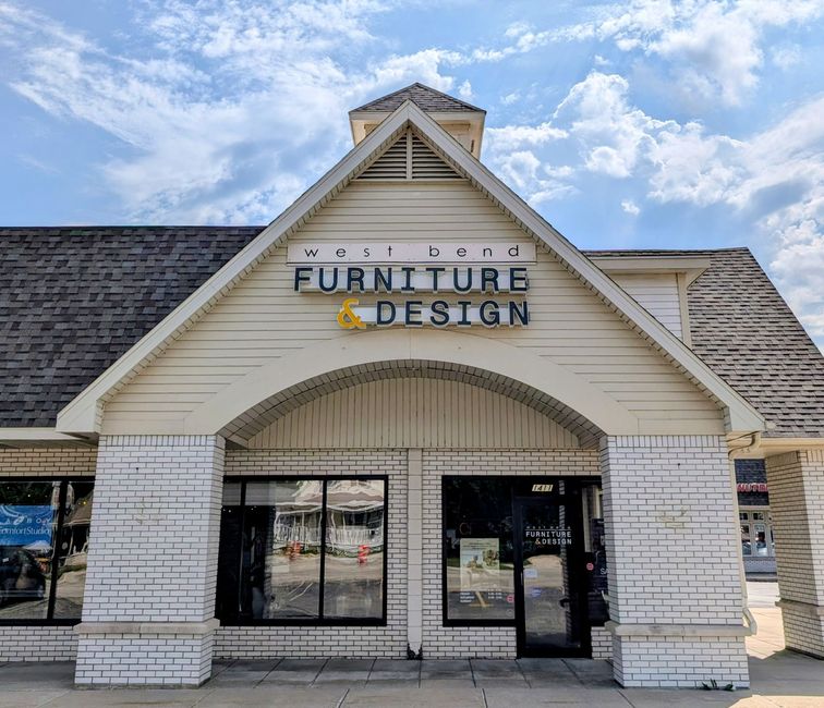 Front entrance of a furniture design store with white brick walls and a peaked roof.