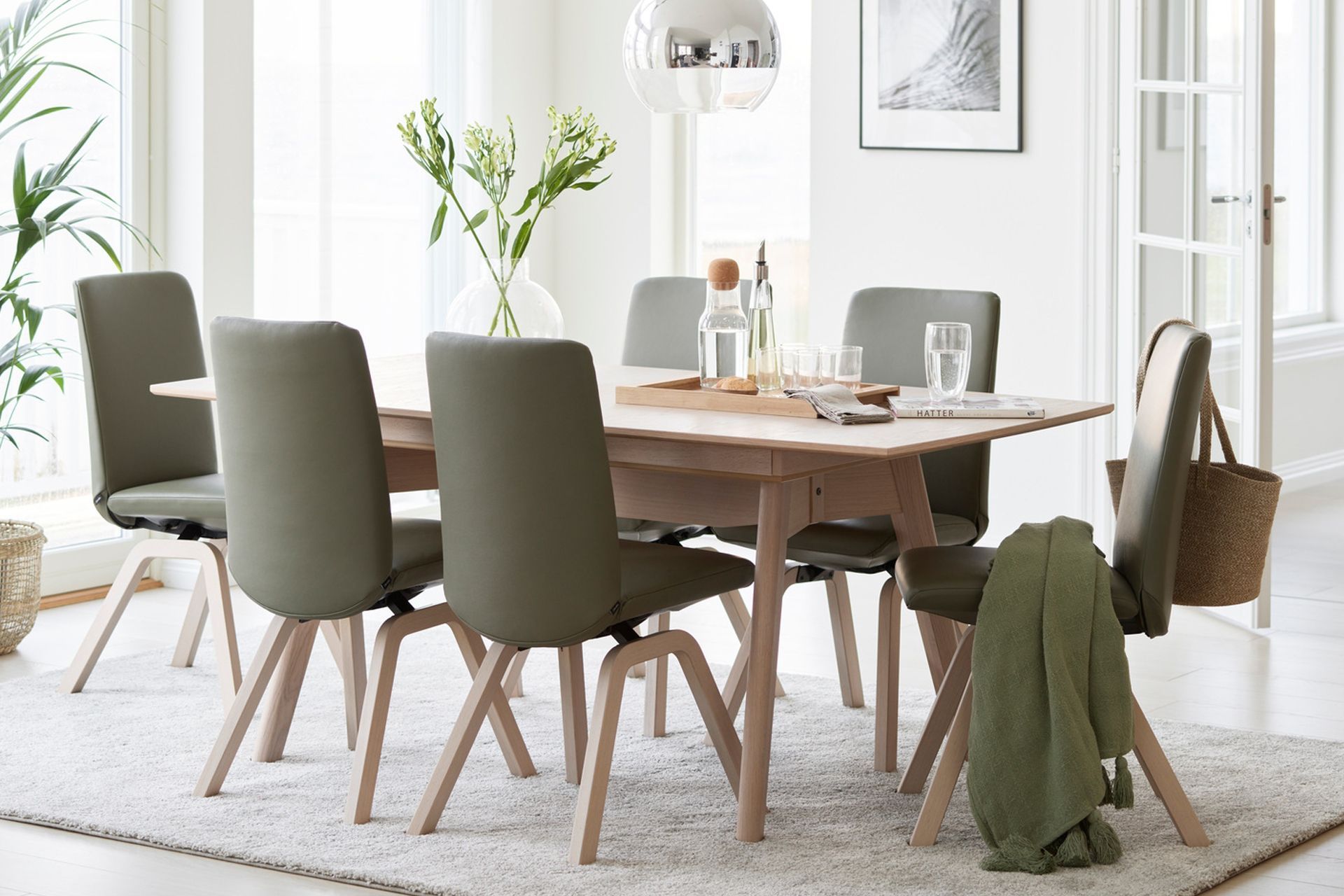 Modern dining room with wooden table, green chairs, and a woven rug in a bright, minimalist interior