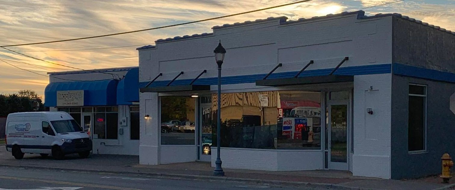 Exterior of businesses on a street, with a delivery van parked in front of one. A lamppost is centered in the view.