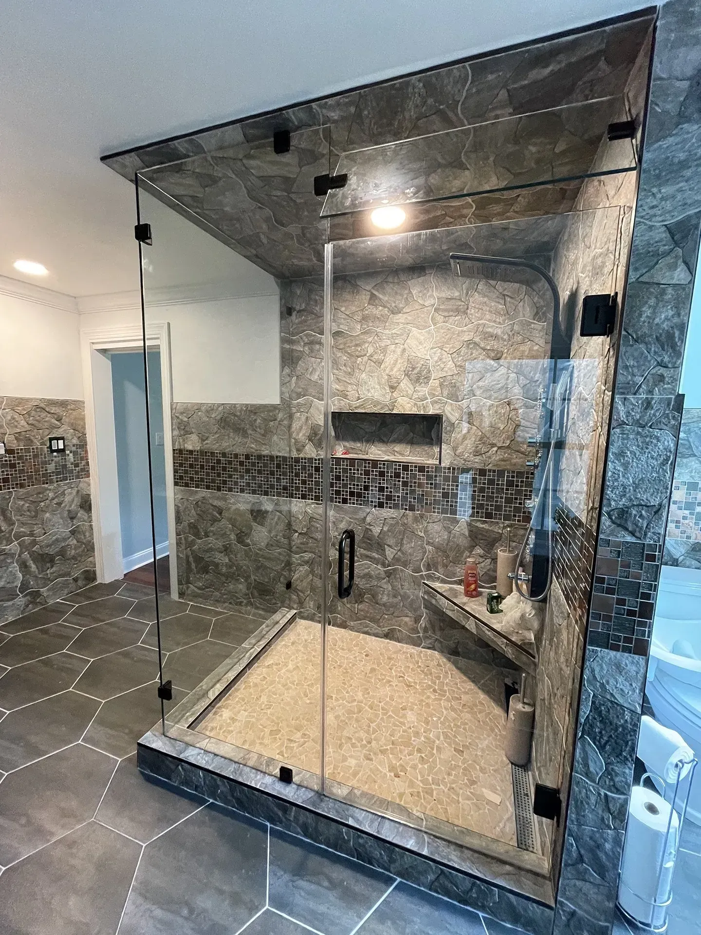 A modern shower with frameless glass doors and dark gray stone walls and floor. The shower has a built-in bench and niche.