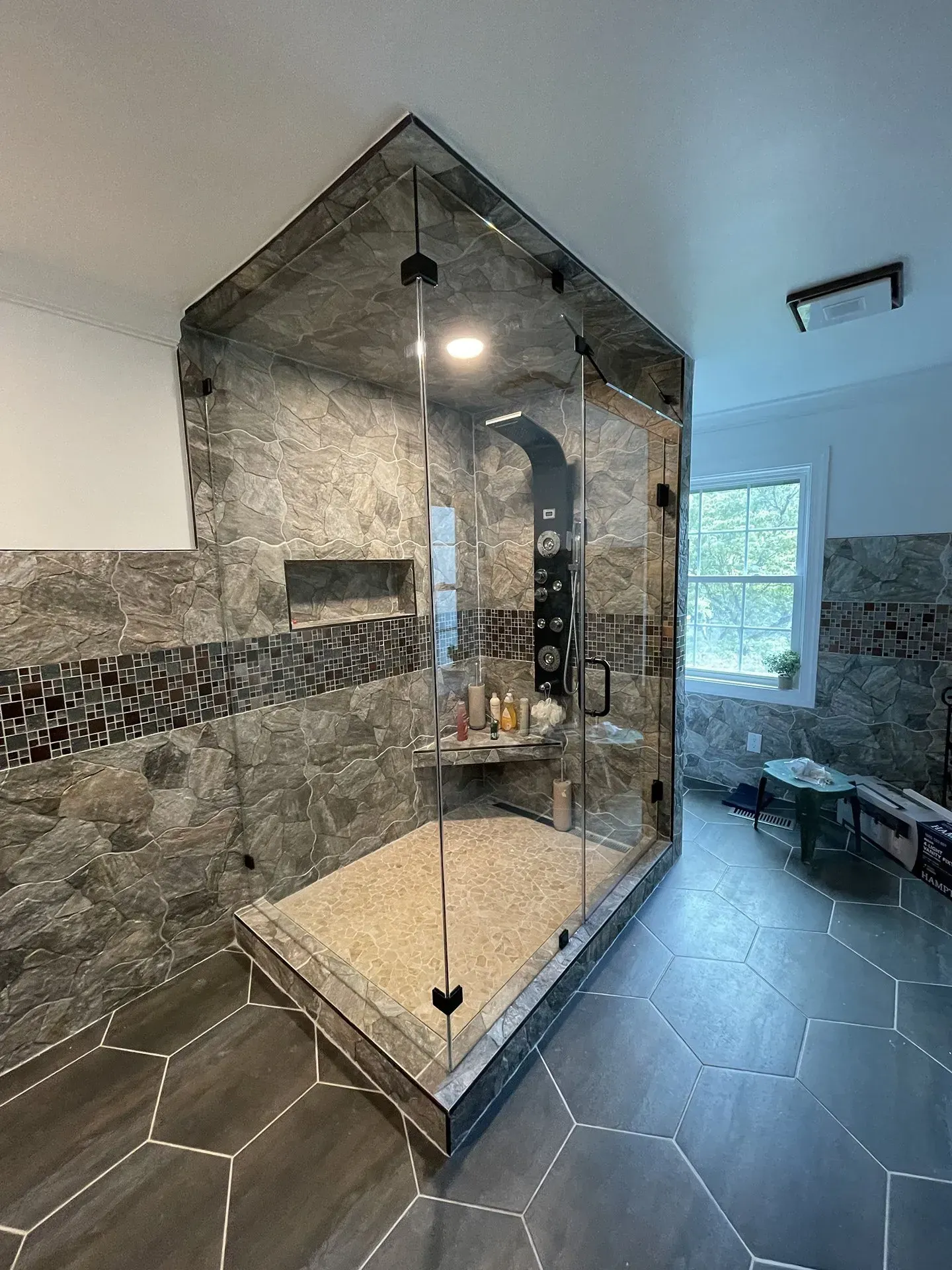Spacious bathroom with a glass-enclosed shower featuring a stone tiled interior, a bench, and pebble flooring.