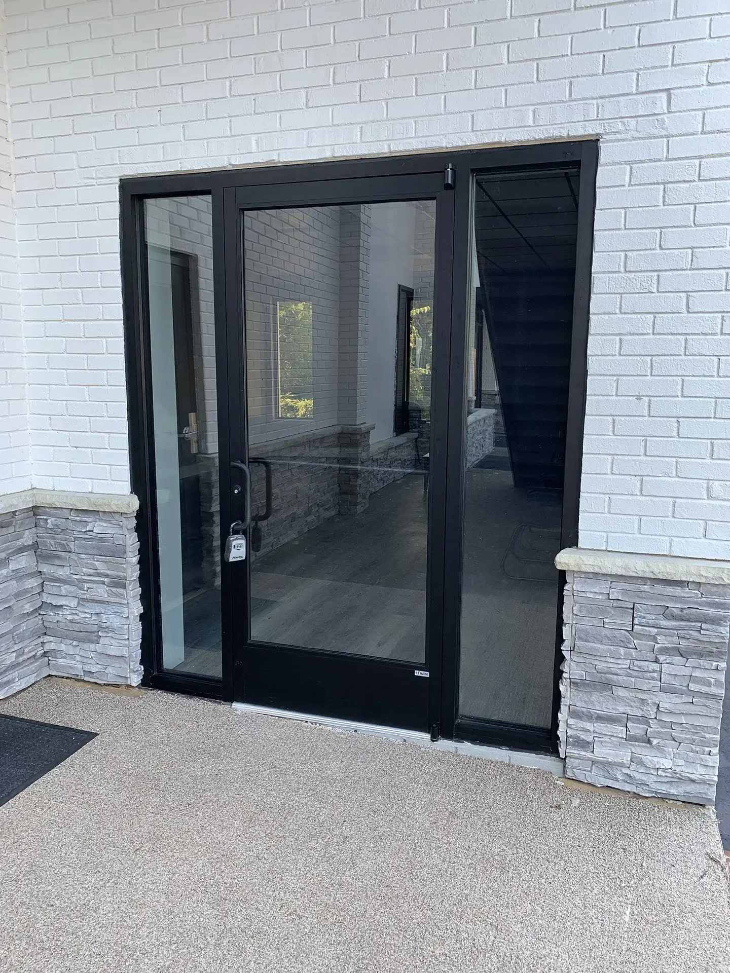 A glass front door with black frame and sidelights set into a white brick facade.