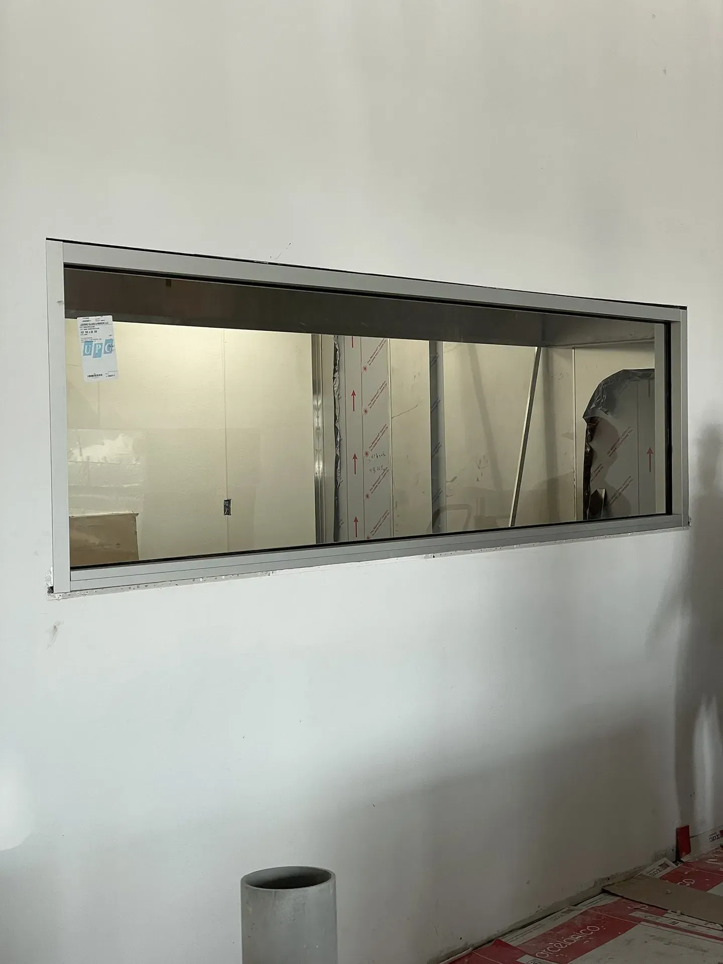 A long, rectangular window in a white wall, revealing a room with construction in progress.
