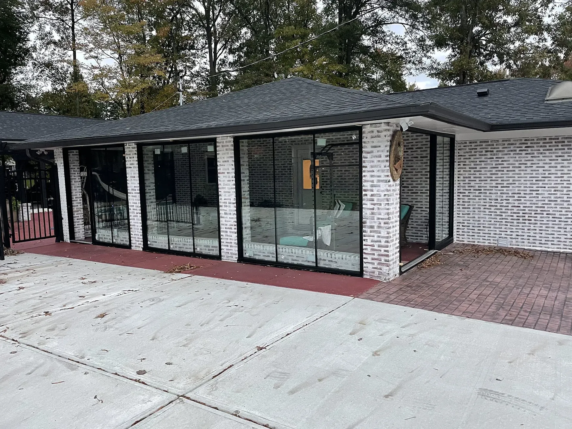 A modern building with black-framed glass walls and a gray brick exterior; a red brick patio is on the right.