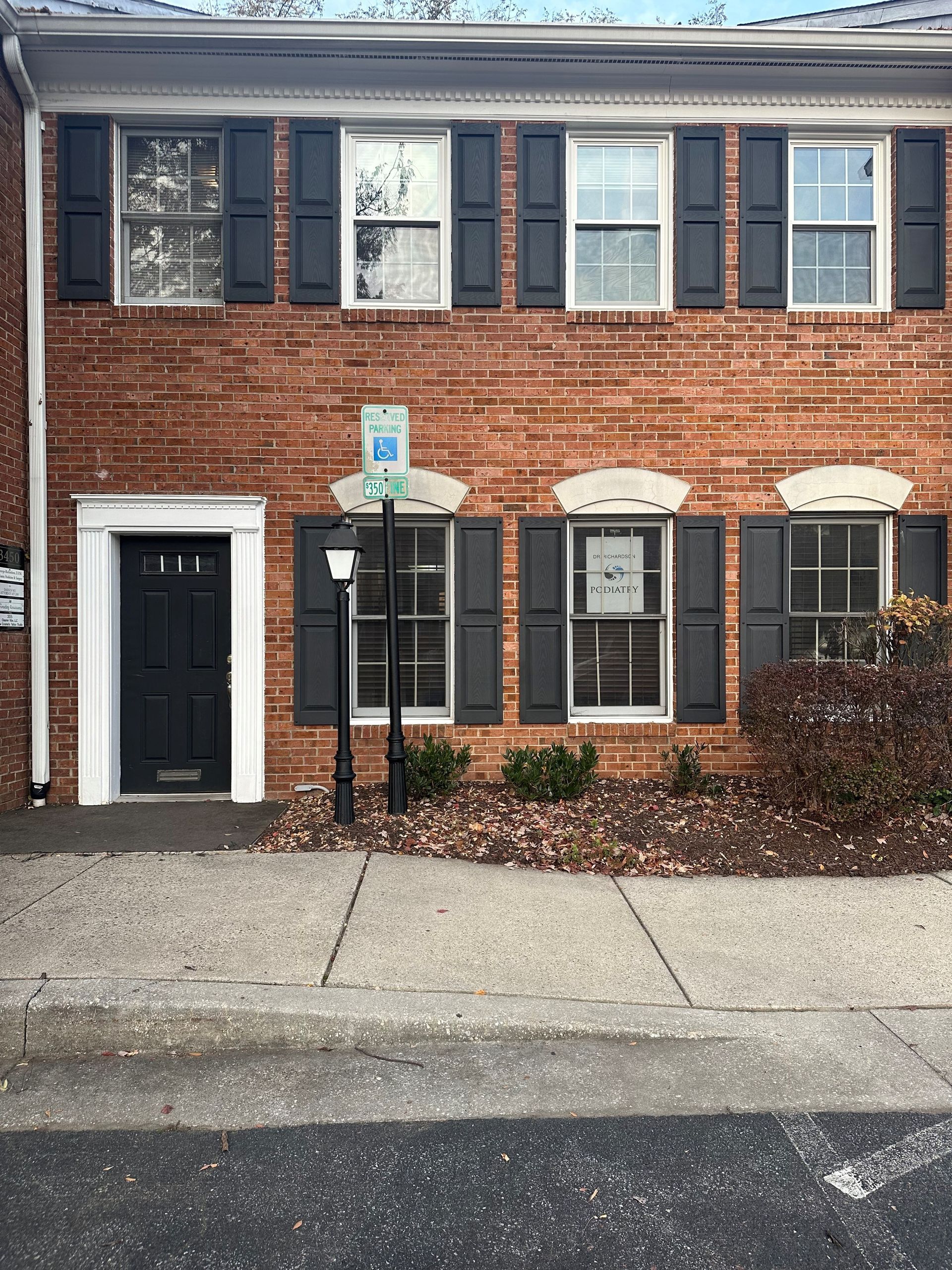 A brick building with black shutters and a handicapped parking spot in front of it.