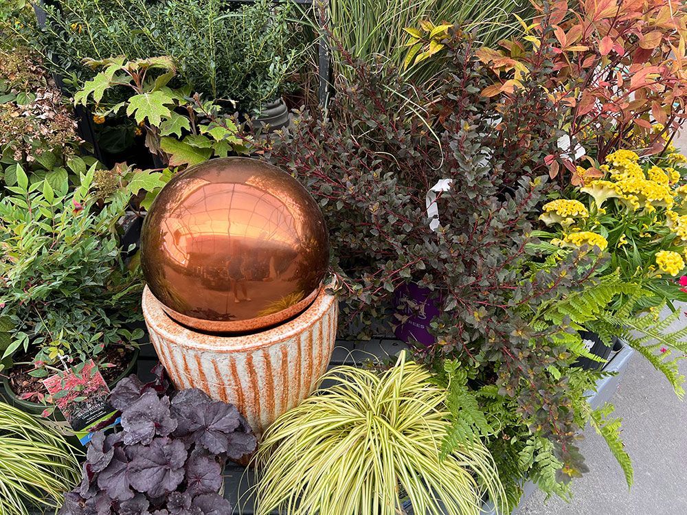 There is a copper ball in the middle of a garden surrounded by plants.