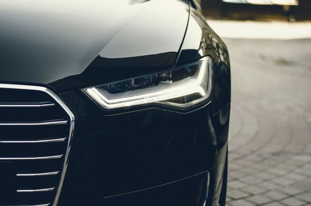 Close-up of a black car’s front headlight and grille on a paved street.