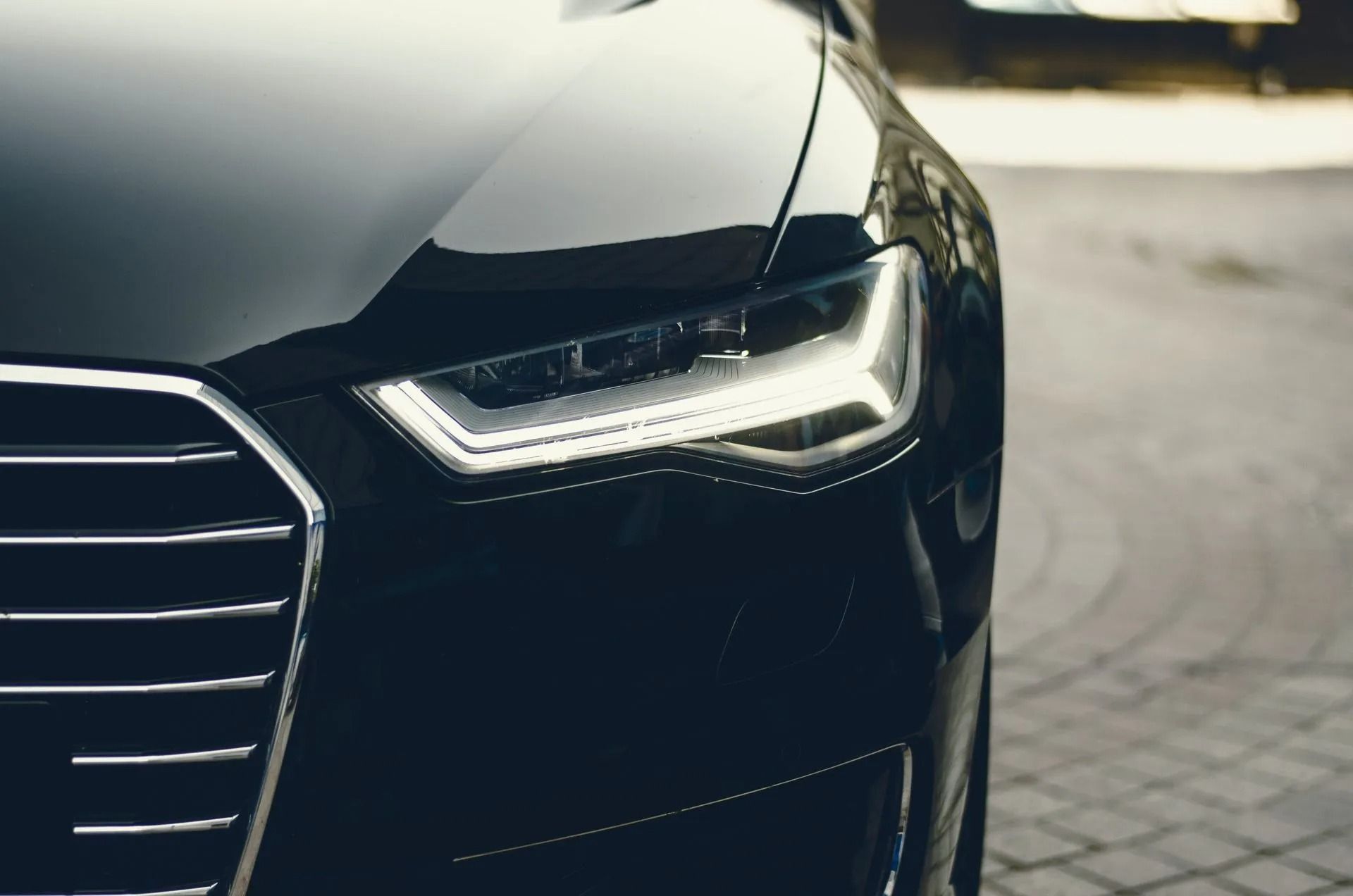 Close-up of a black car’s front headlight and grille on a paved street.