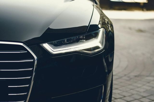 Close-up of a black car’s front headlight and grille on a paved street.