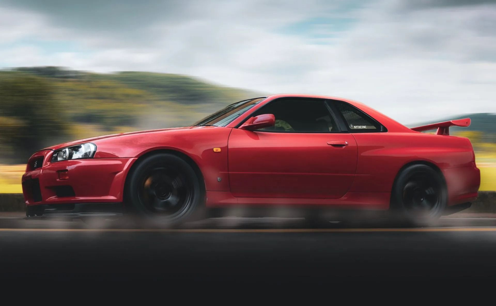 Red sports coupe speeding on a blurred road with a mountainous backdrop