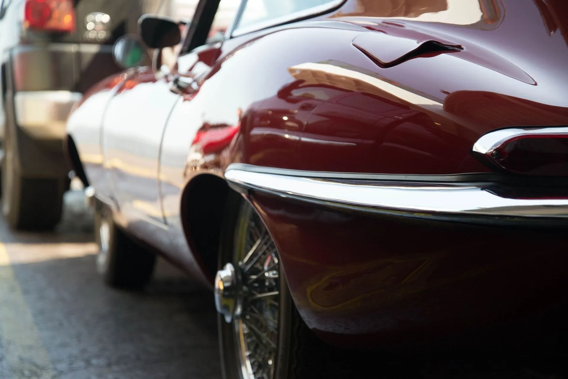 Close-up of a red vintage car’s side and rear wheel, parked on a street at sunset