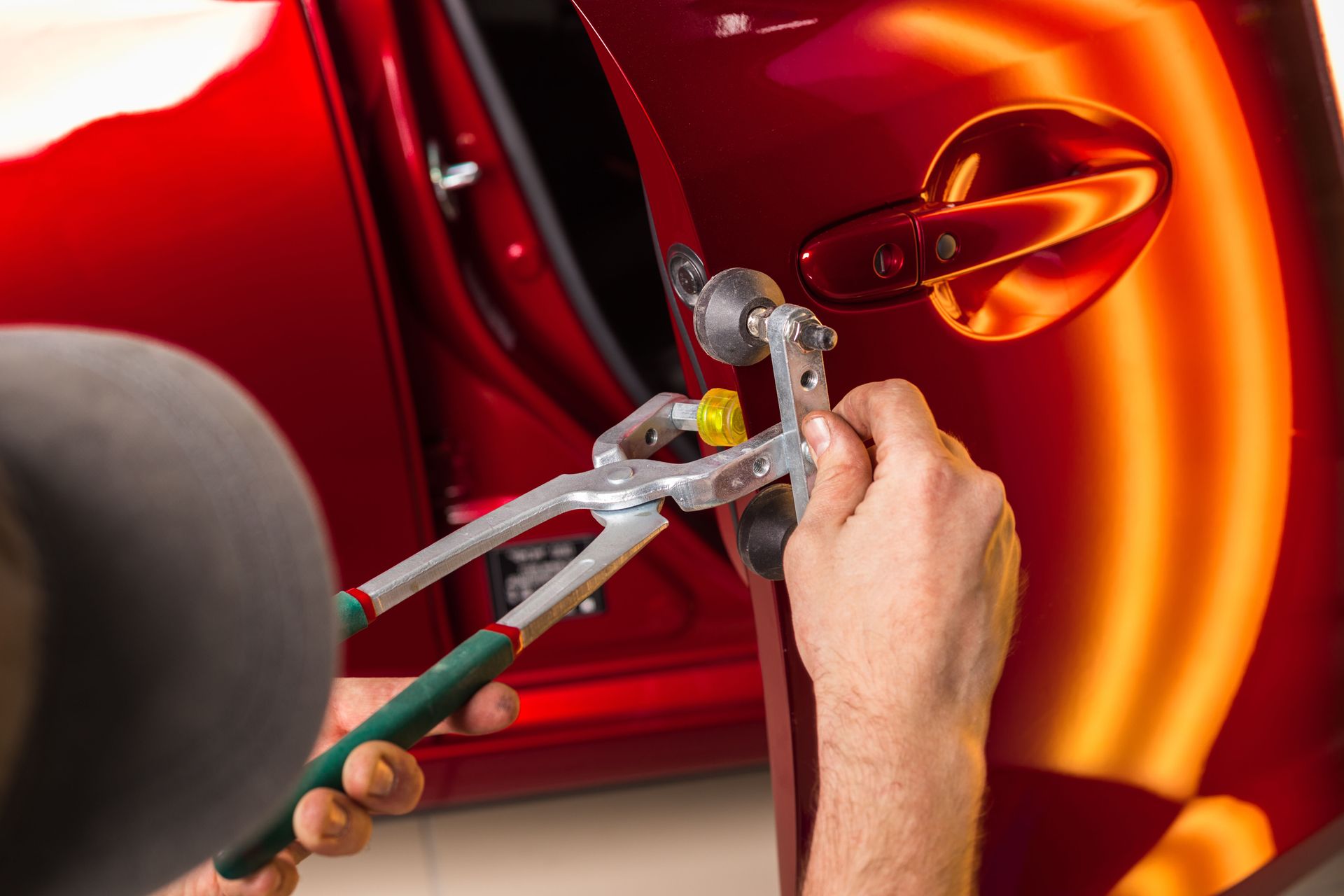 Mechanic using pliers to repair a red car’s door handle and wheel area