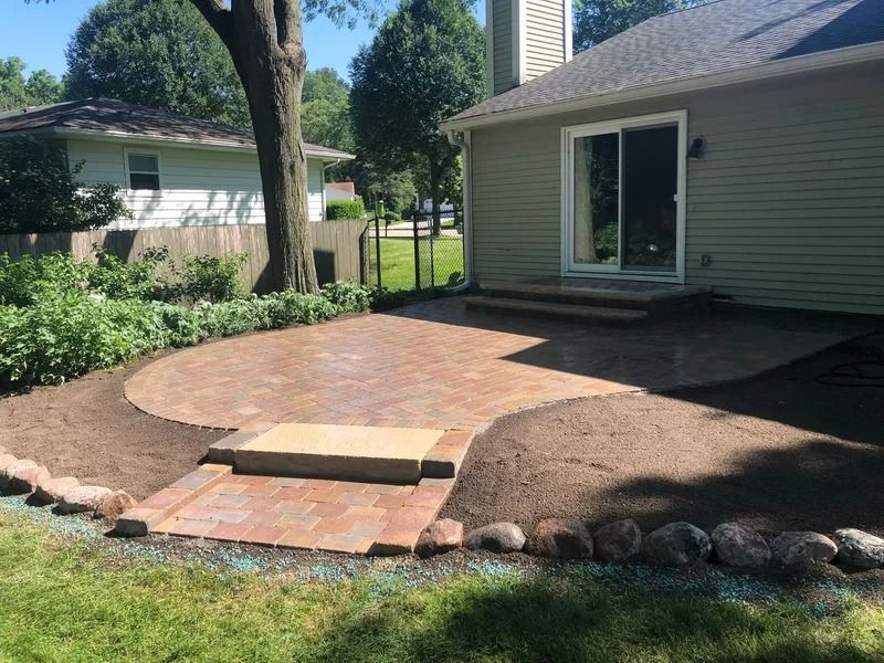 Backyard patio with brick step, curved paver area, and garden beds beside a house
