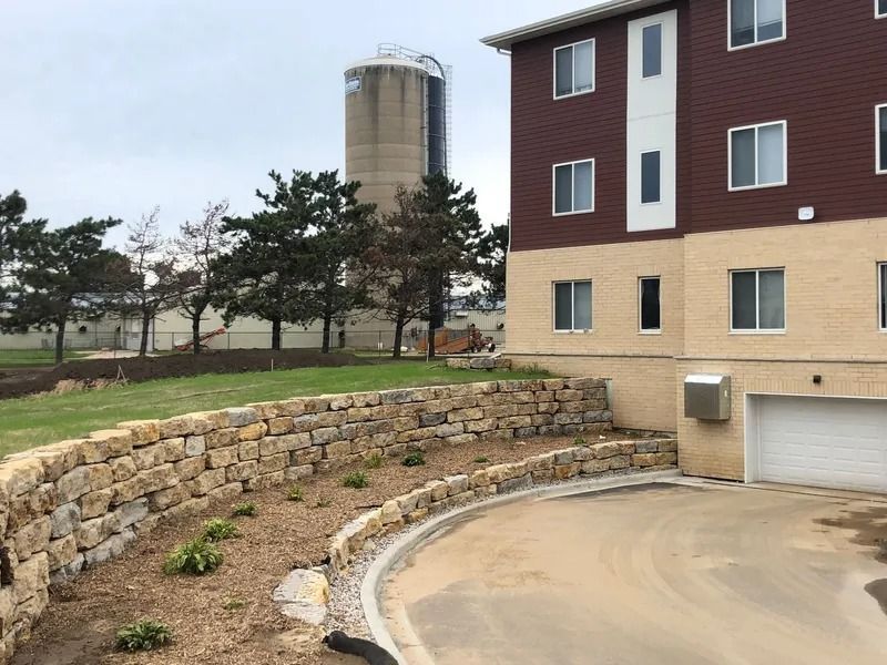 Residential building with garage, stone retaining wall, and distant silo on a cloudy day